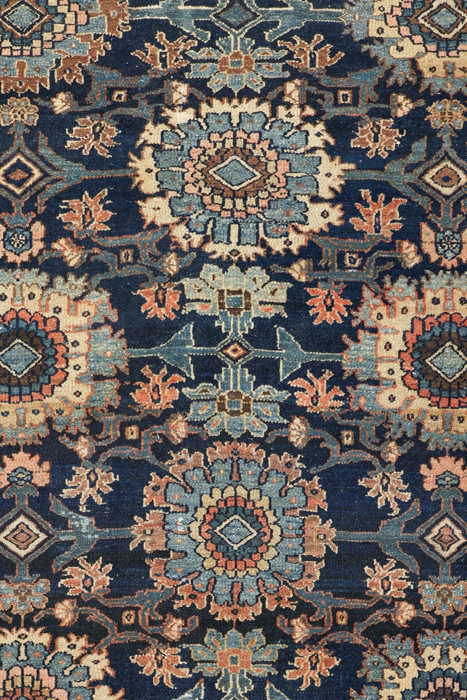 Intricate detail of a handwoven tribal rug in navy, featuring floral and geometric patterns in muted peach and teal.
