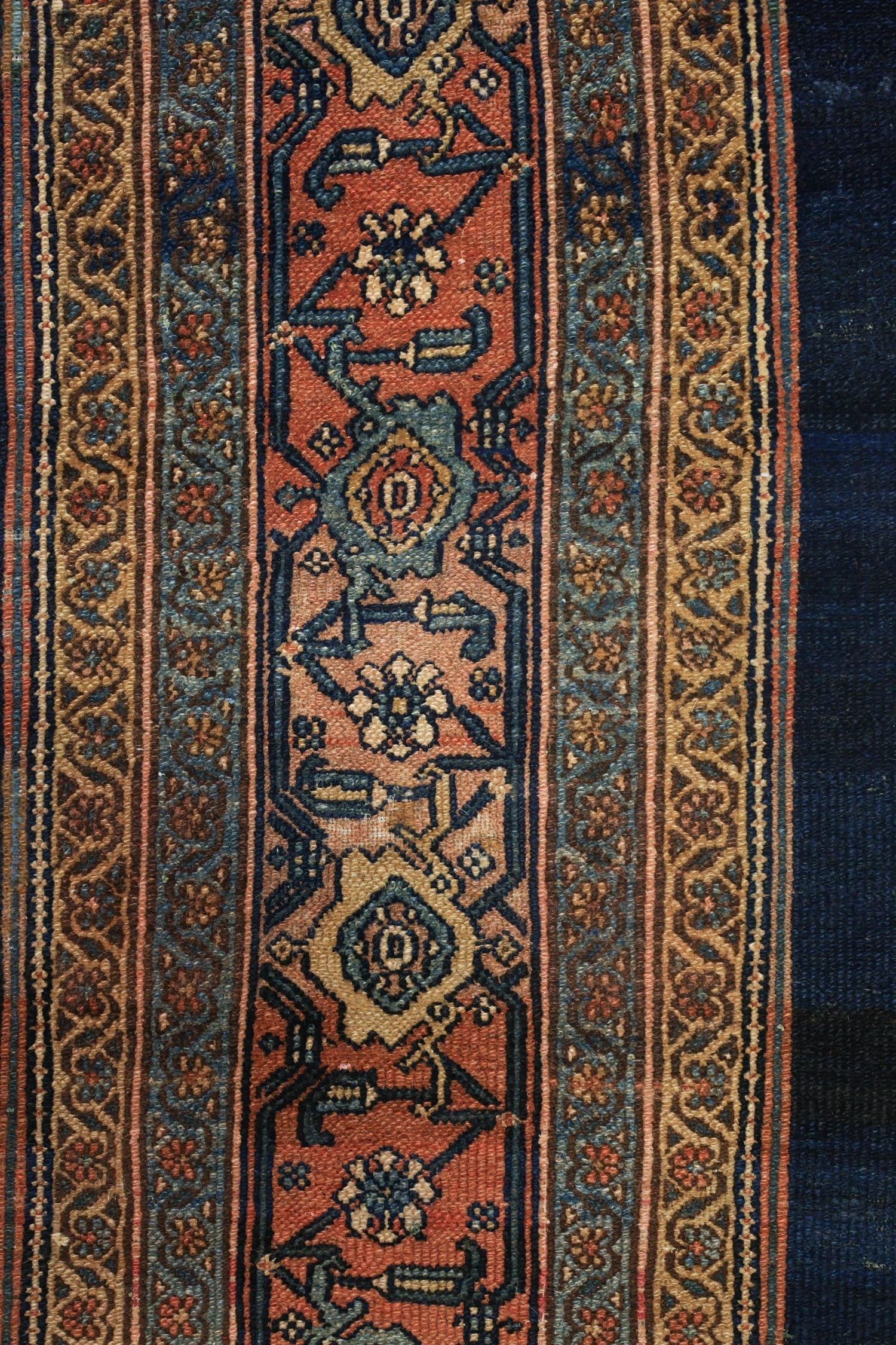 Detail of antique rug's handwoven border, showcasing intricate floral and geometric patterns in muted blues, reds, and browns.
