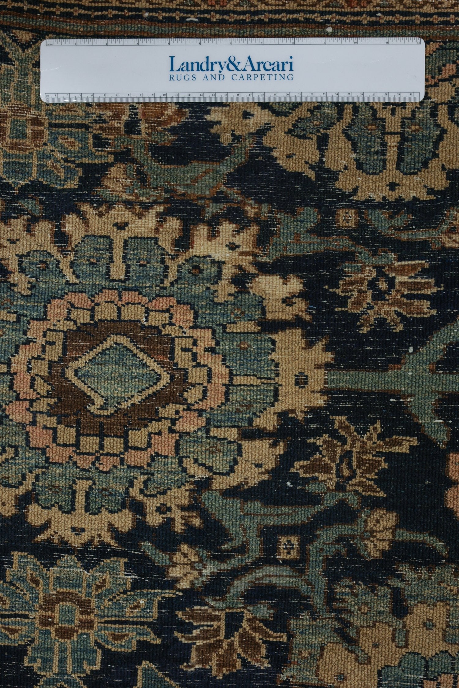 Detailed close-up of antique tribal rug's handwoven texture, showcasing intricate teal, beige, and brown patterns.
