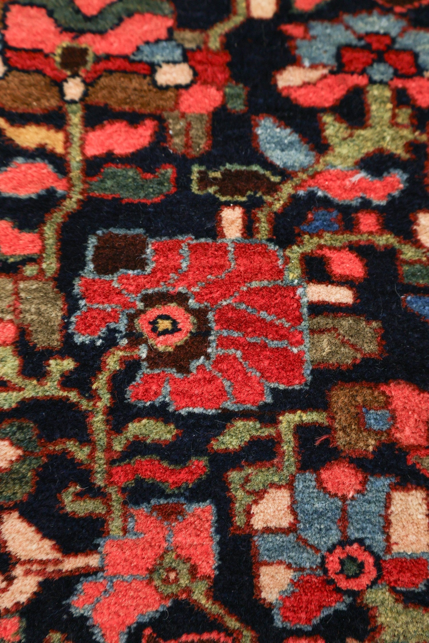 Close-up of a richly colored antique rug, showcasing intricate handwoven details in red, blue, and beige tones.
