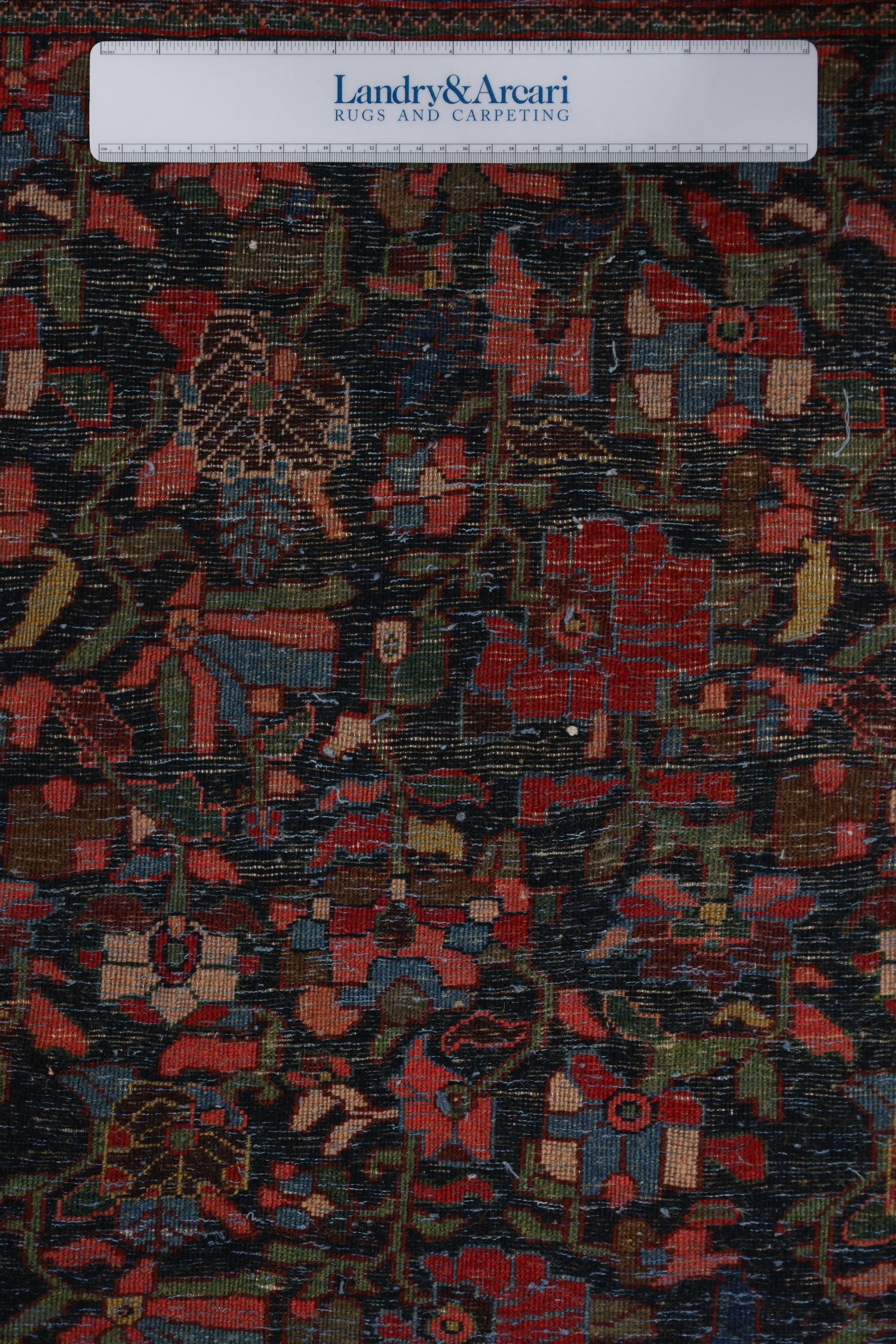 Close-up detail of an antique Bijar rug's handwoven pattern, showcasing rich reds, blues, and greens on a dark background.
