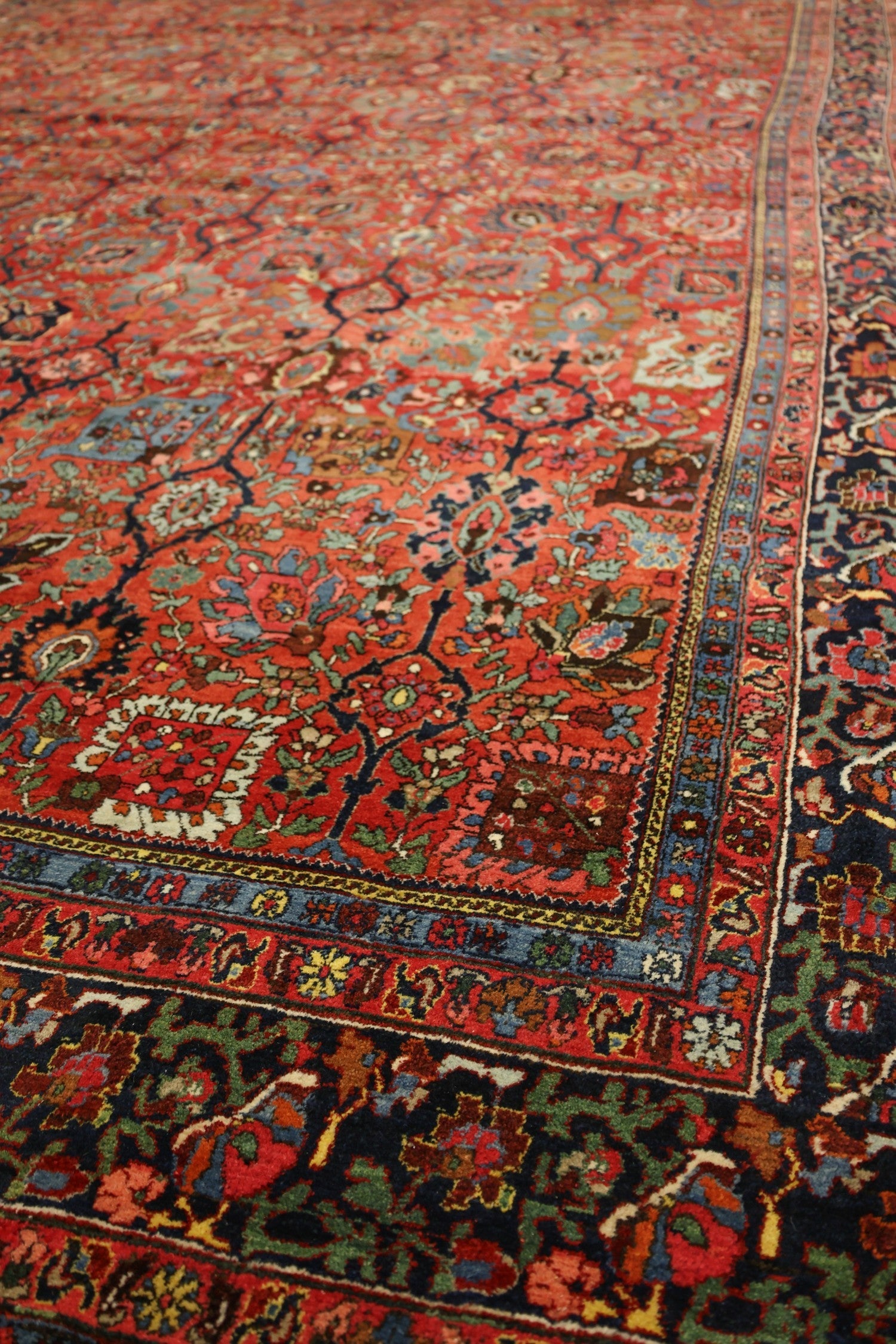 Intricate handwoven rug detail, showcasing a vibrant red and blue floral pattern with a rich, dark border.
