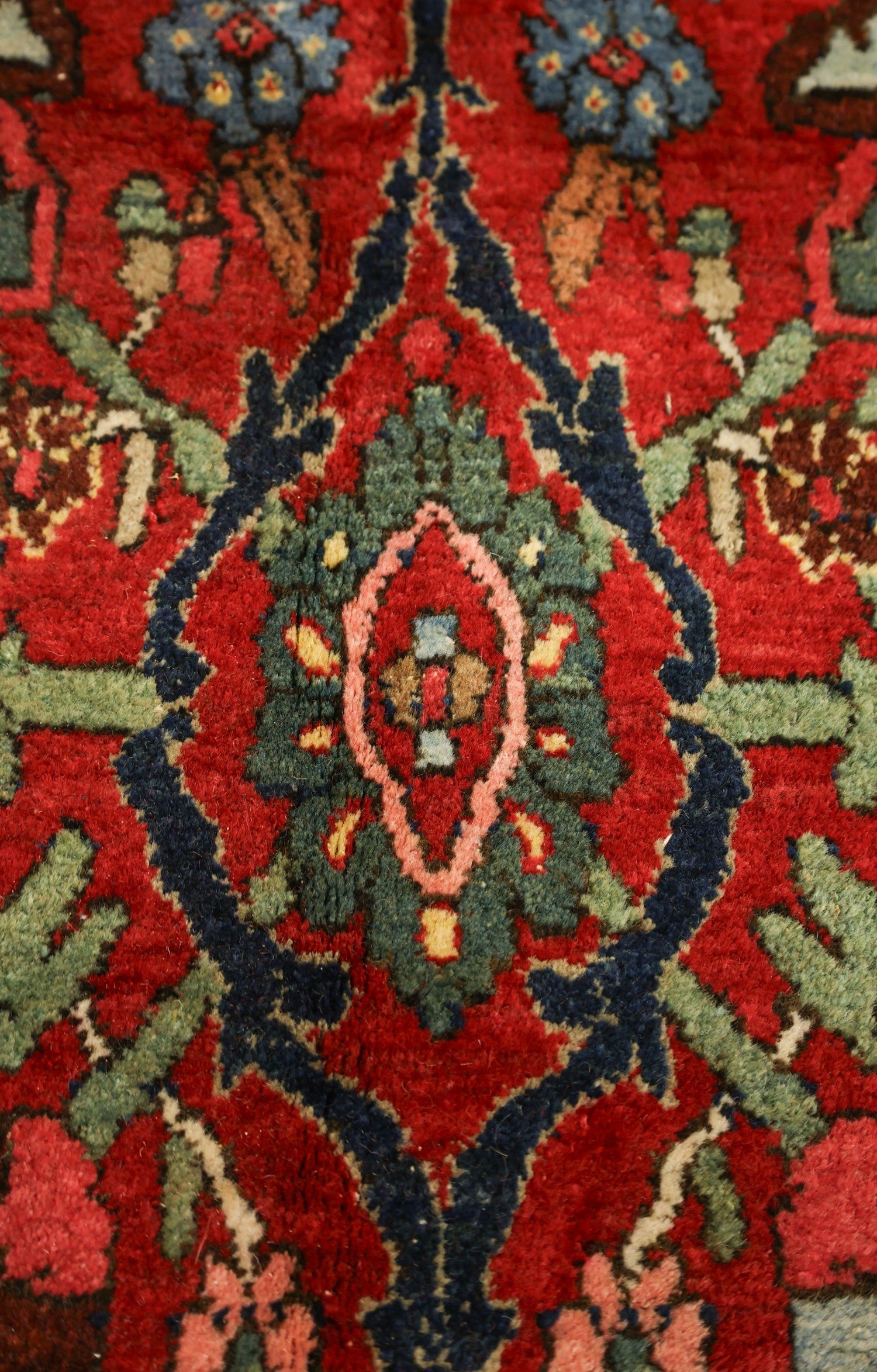 Close-up of antique rug's intricate, handwoven floral pattern in rich reds, blues, and greens.
