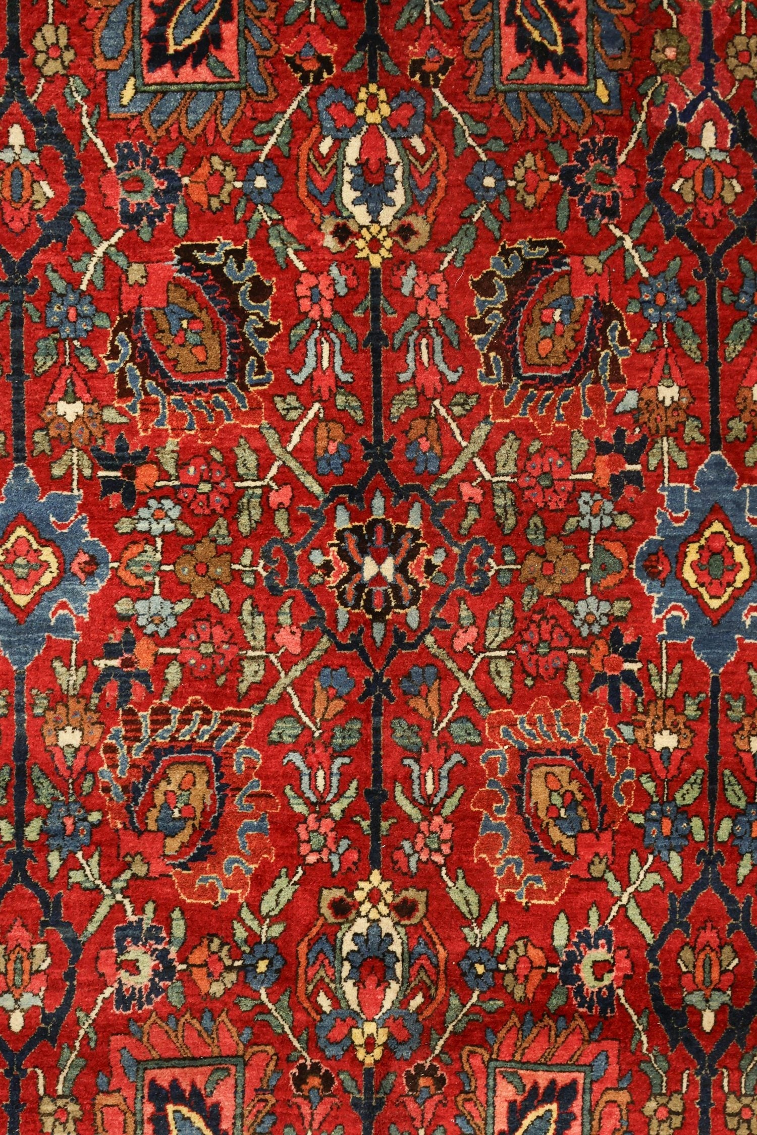 Intricate detail of a red antique rug with floral and geometric patterns in blue, green, and brown.
