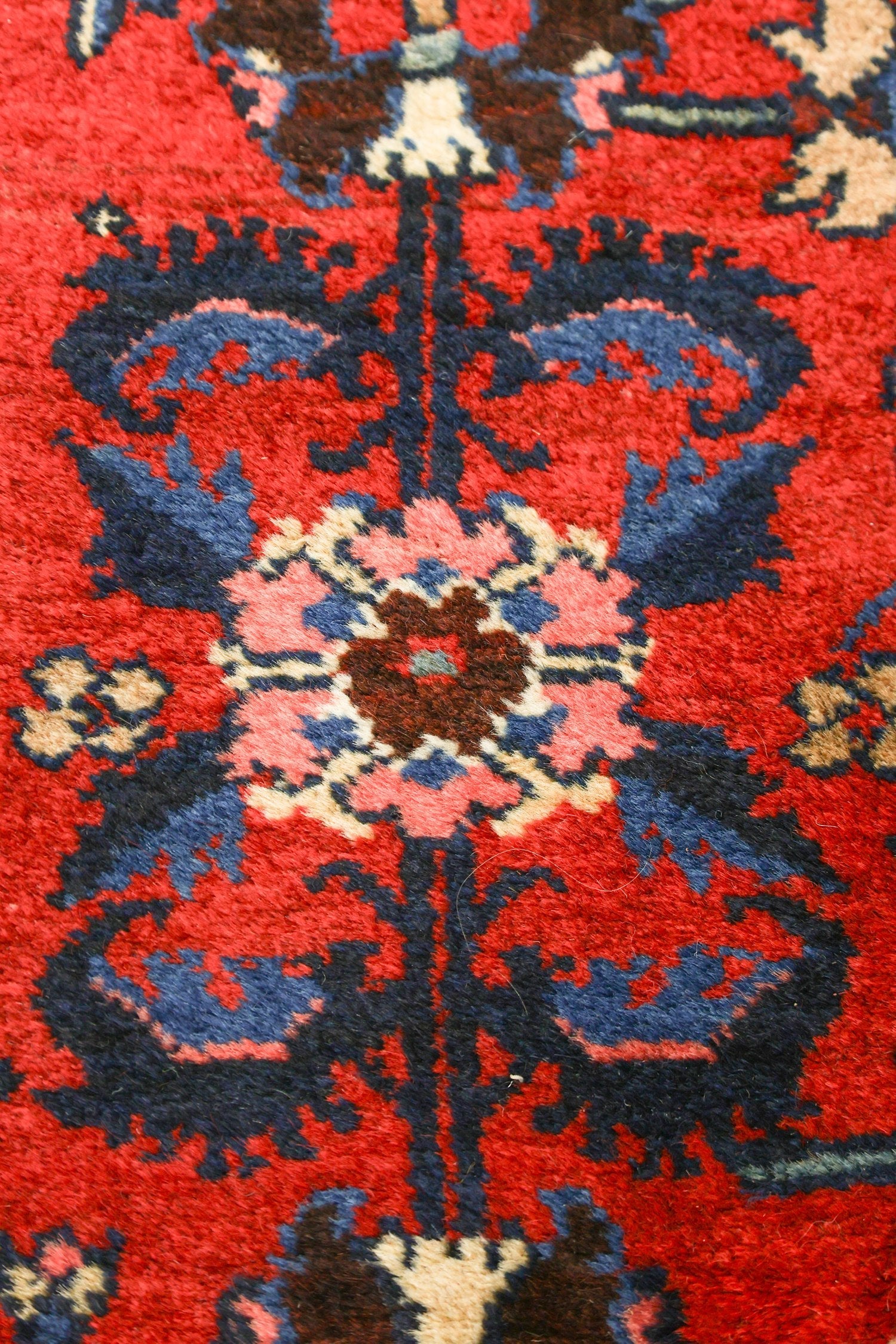 Close-up of antique rug detail: vibrant red base with intricate navy, pink, and beige floral pattern.
