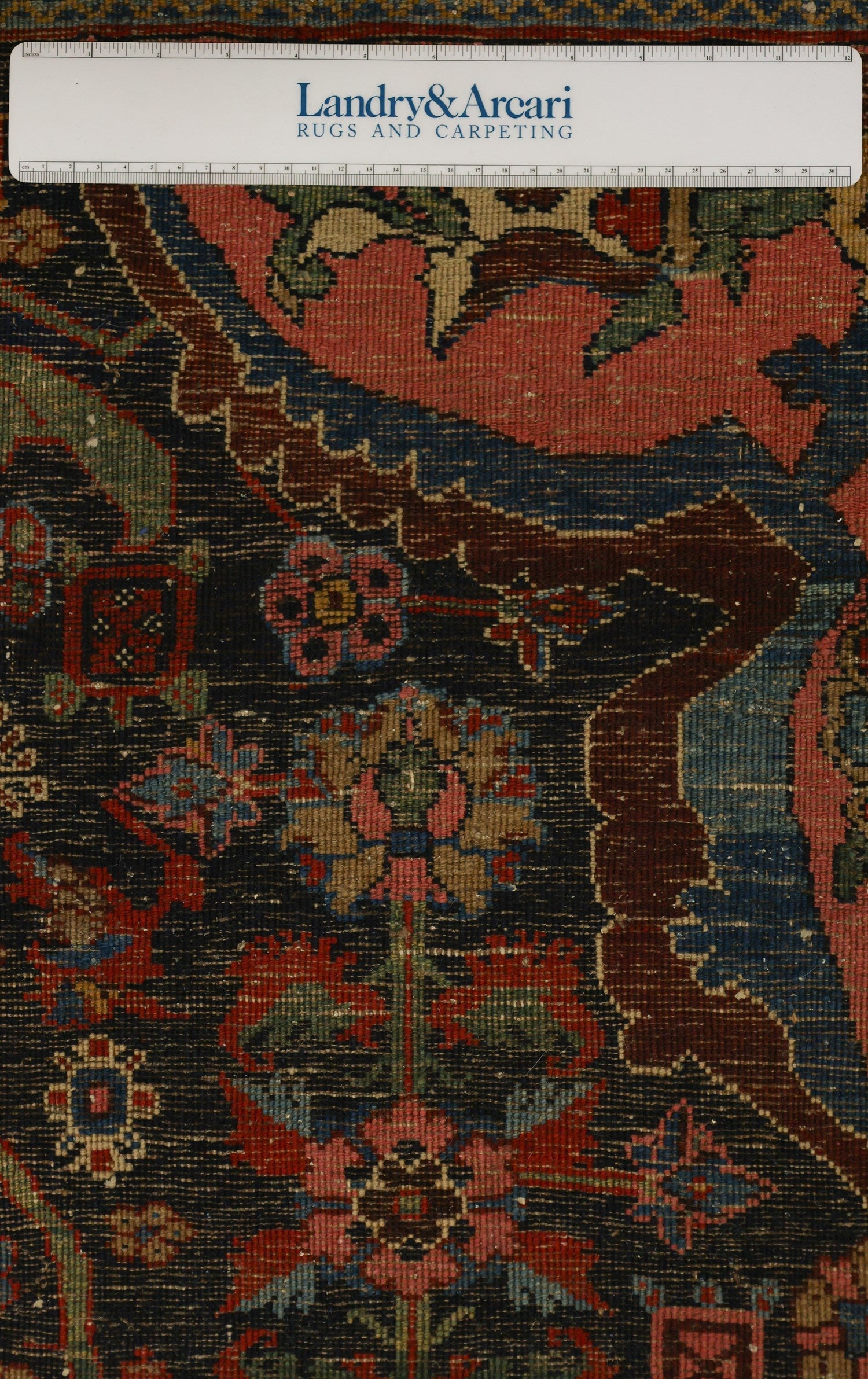 Close-up detail of an antique Bijar rug's intricate, handwoven floral pattern in rich reds, blues, and greens on a dark background.
