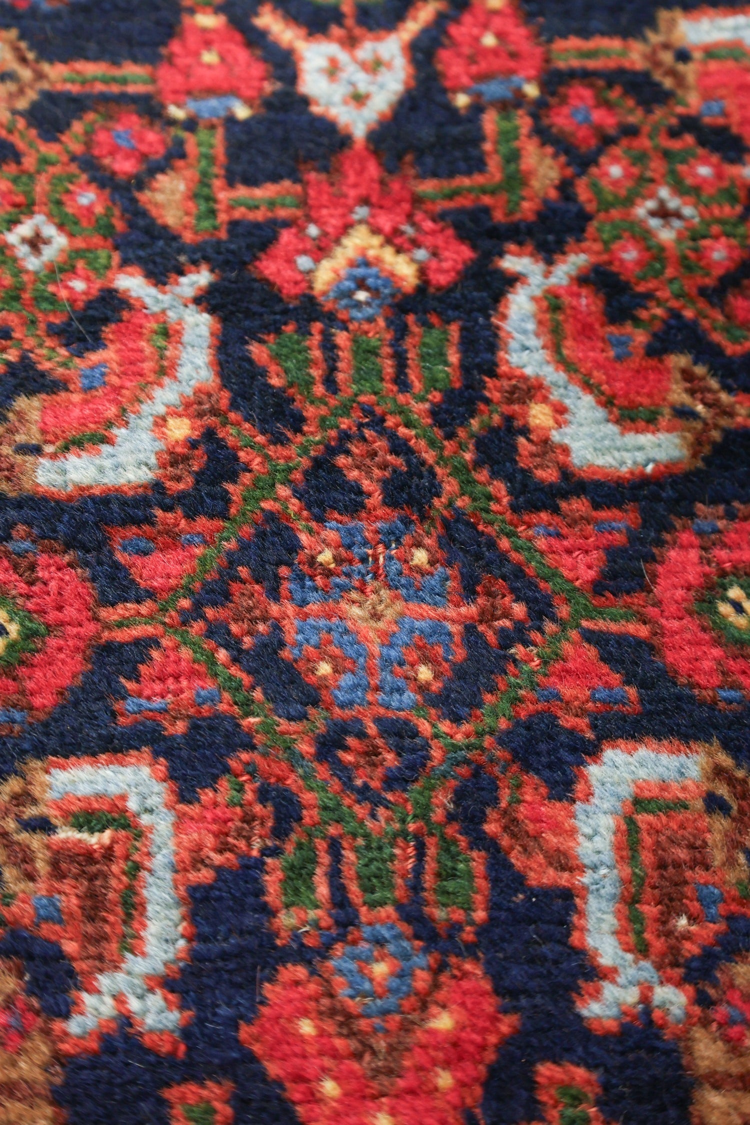 Close-up of richly colored, handwoven rug detail; intricate pattern in reds, blues, and greens.
