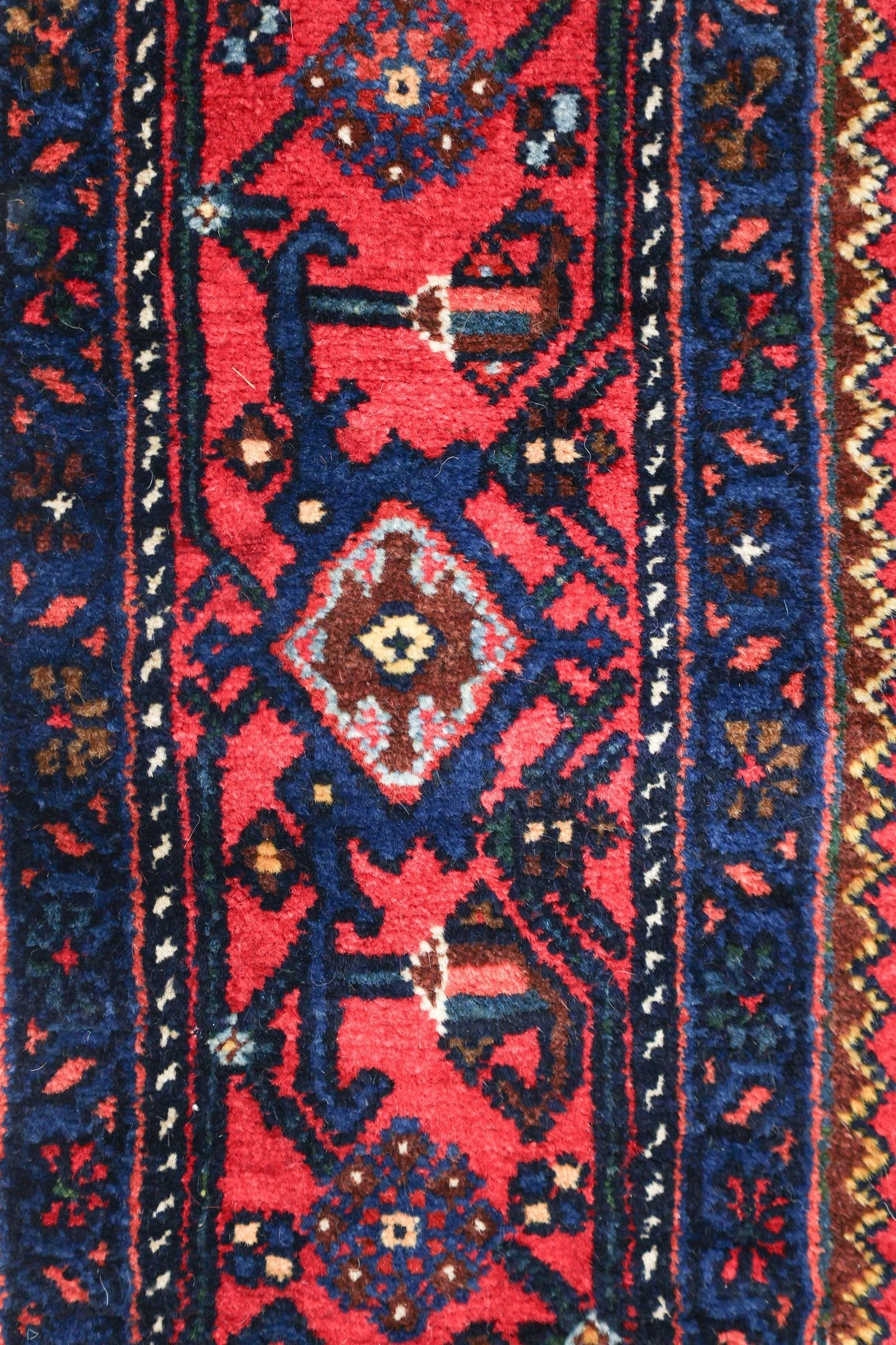 Detail of antique rug's handwoven, red and navy tribal pattern.
