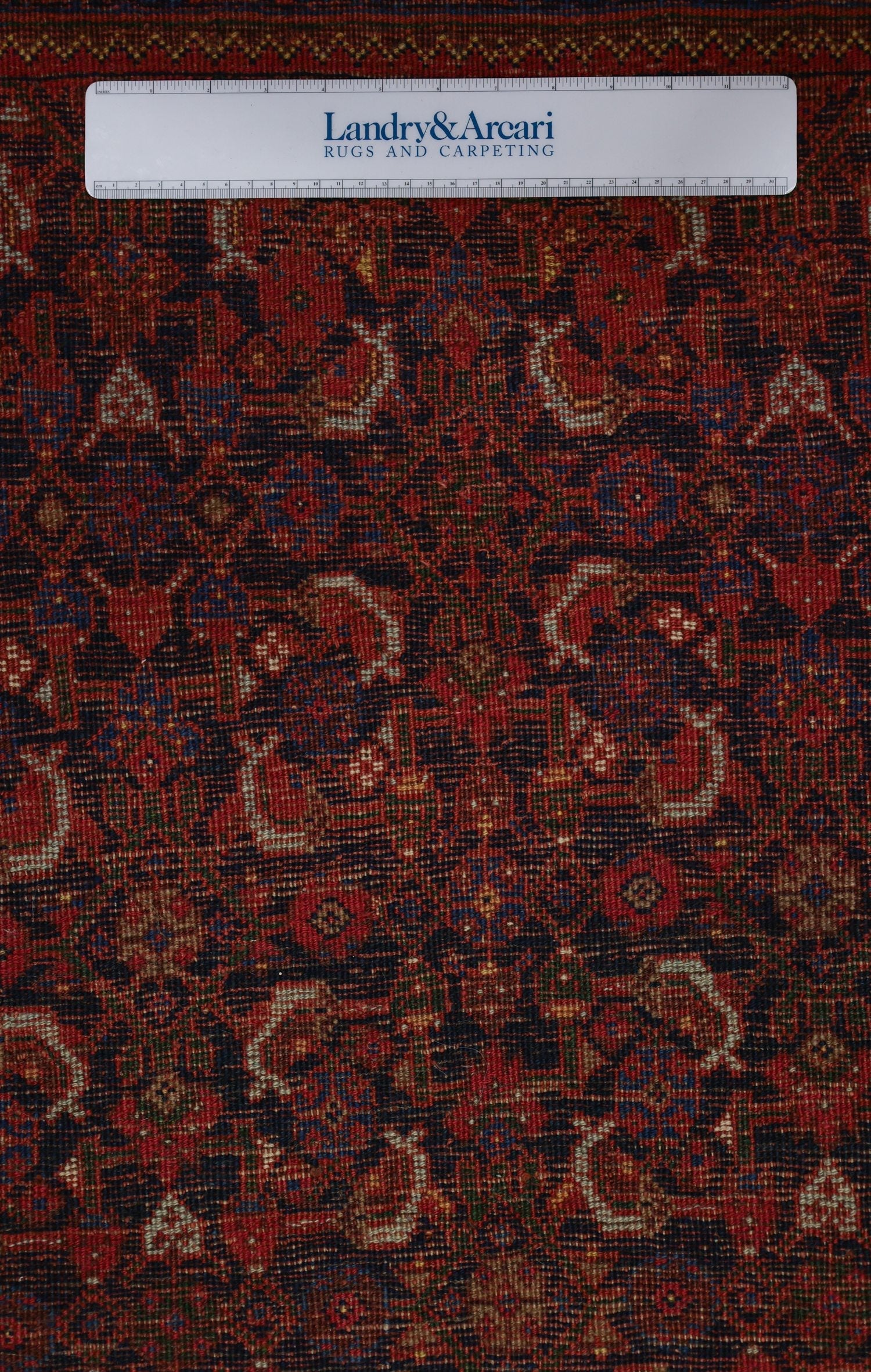 Close-up detail of a handwoven rug, showcasing intricate red and navy floral pattern.
