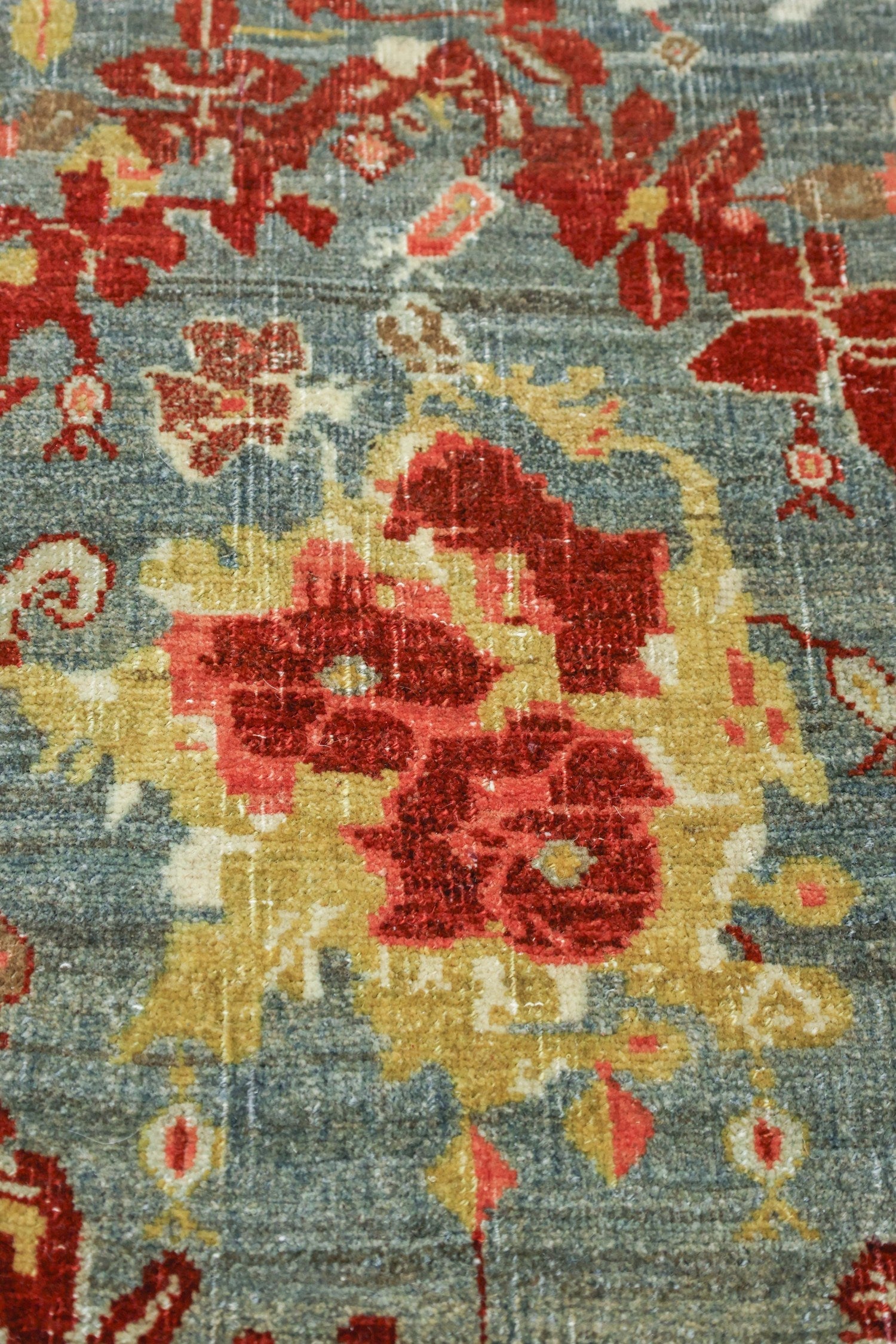 Close-up detail of a handwoven rug with a gray background and red and gold floral pattern.
