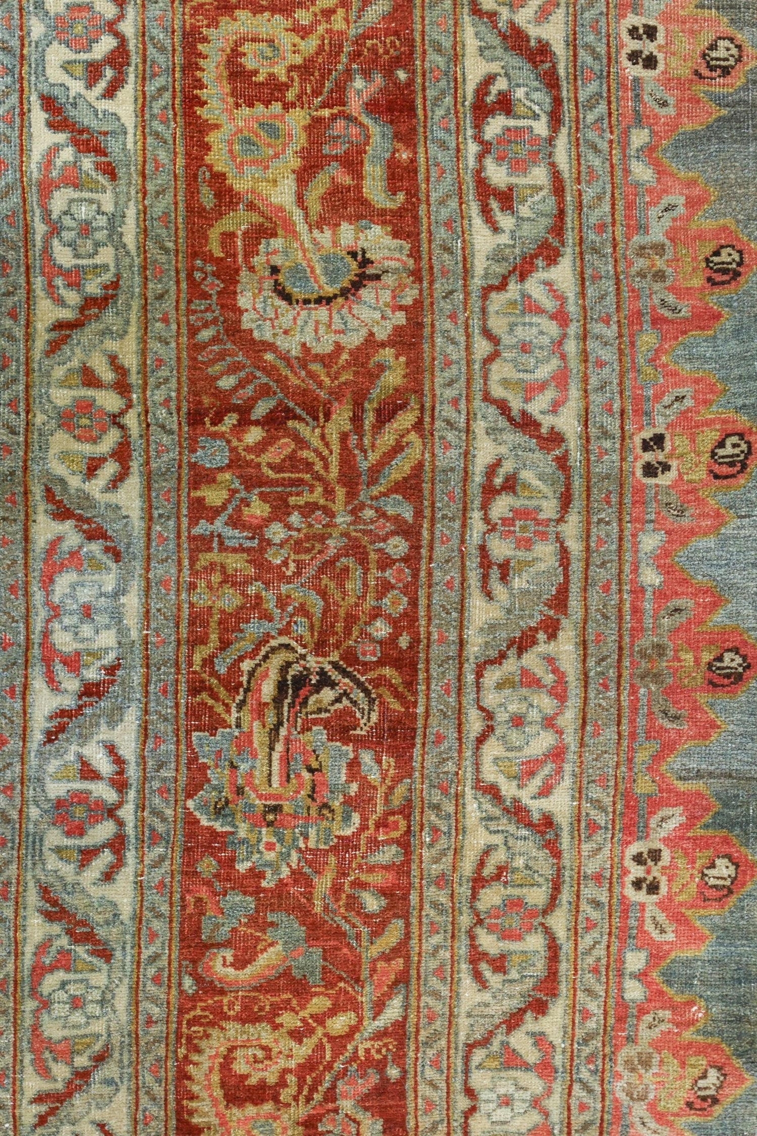 Detail of antique rug's handwoven floral pattern in red, beige, and blue.
