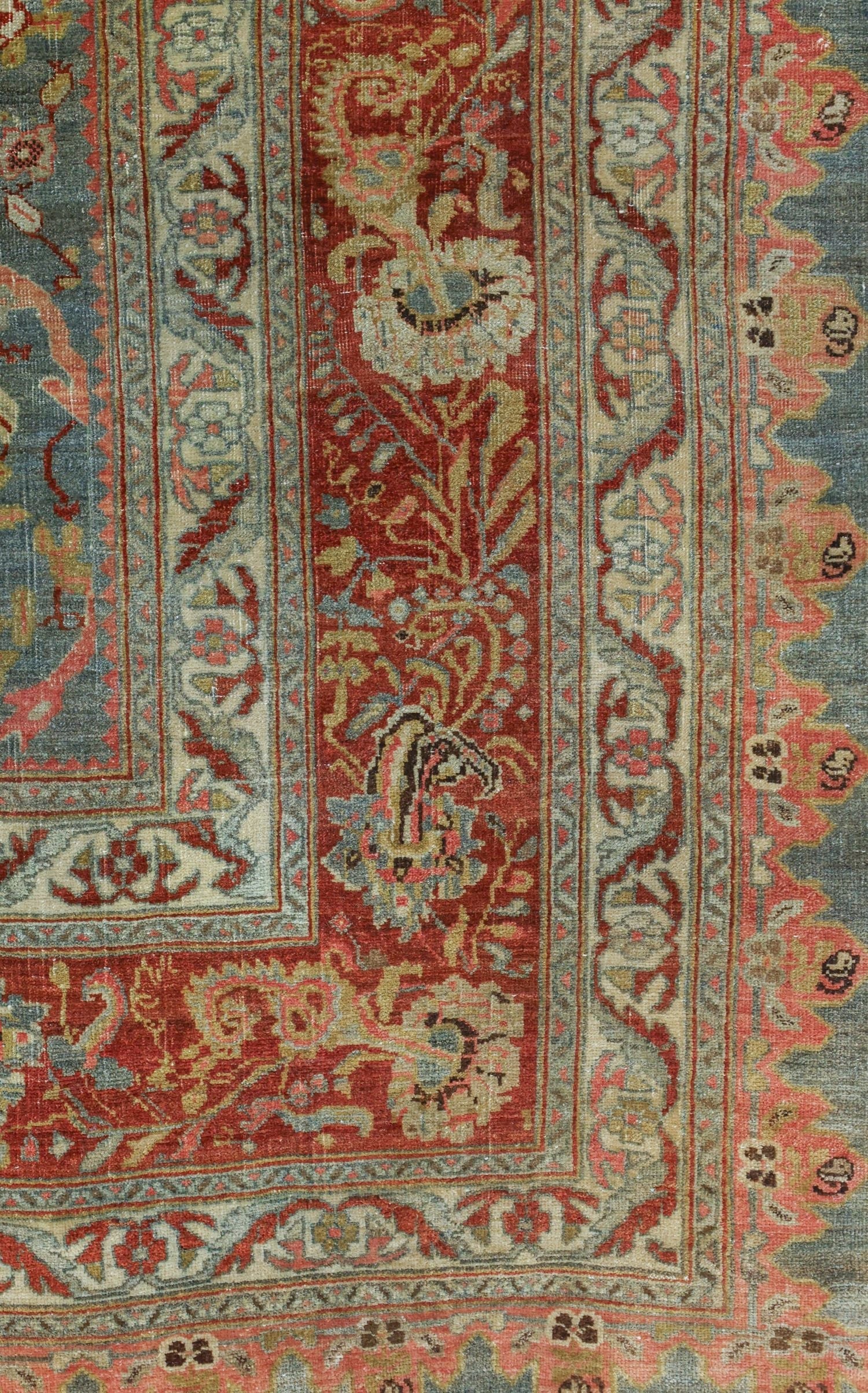 Detailed close-up of an antique rug's border, showcasing intricate floral and geometric patterns in muted reds, blues, and creams.
