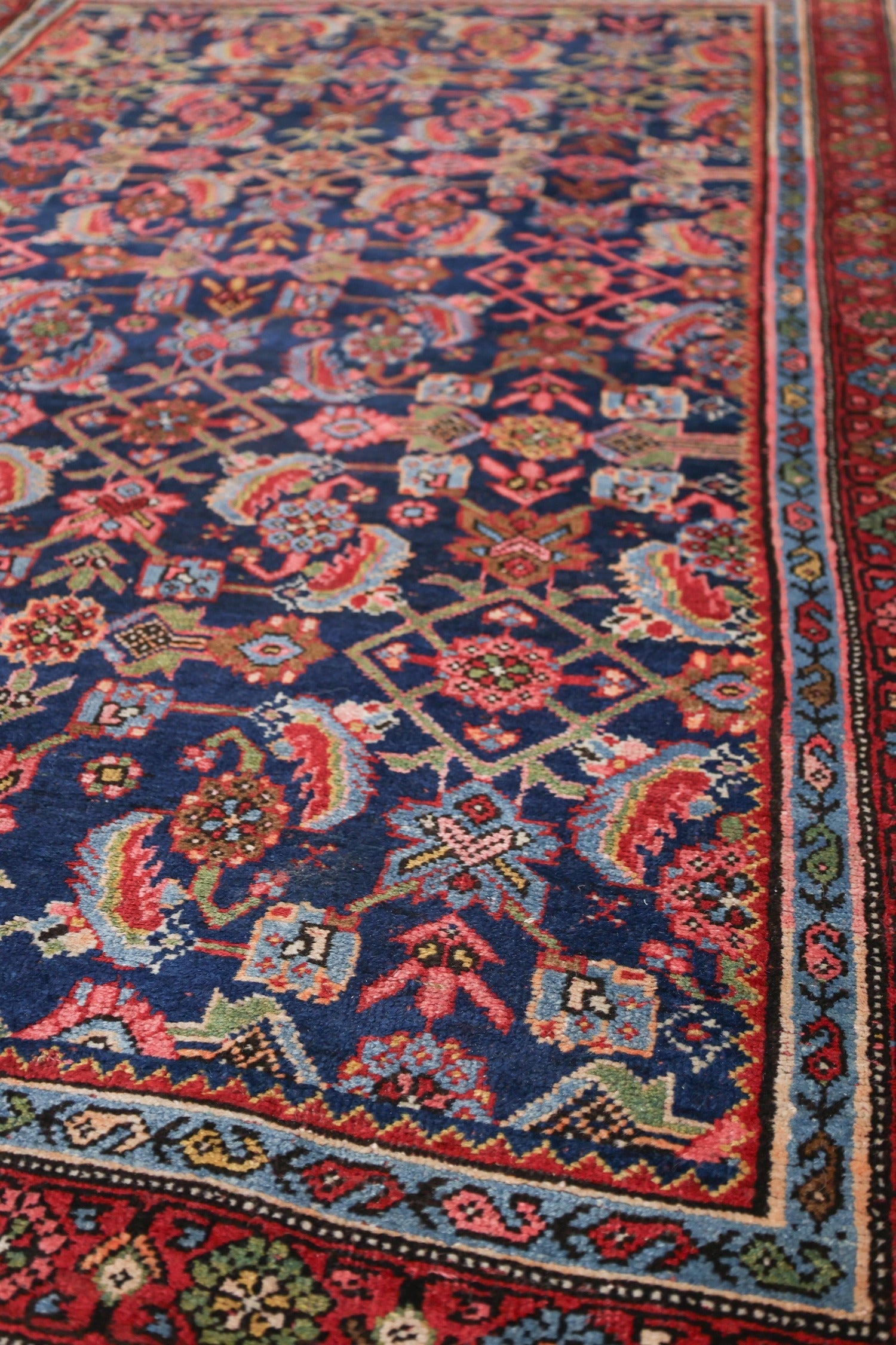 Detailed close-up of a handwoven rug with a navy blue field and intricate floral pattern in red, pink, and blue.
