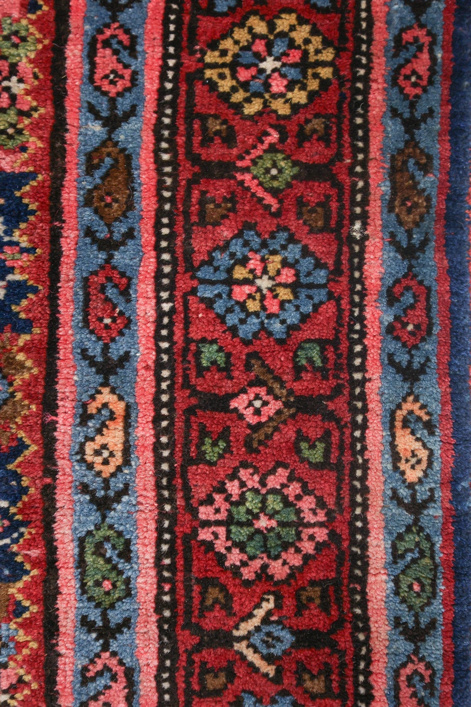 Close-up of a handwoven rug's detailed floral pattern in red, blue, and pink hues.
