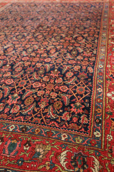 Detail of antique Bijar rug, showcasing intricate red and navy floral pattern with a patterned border.
