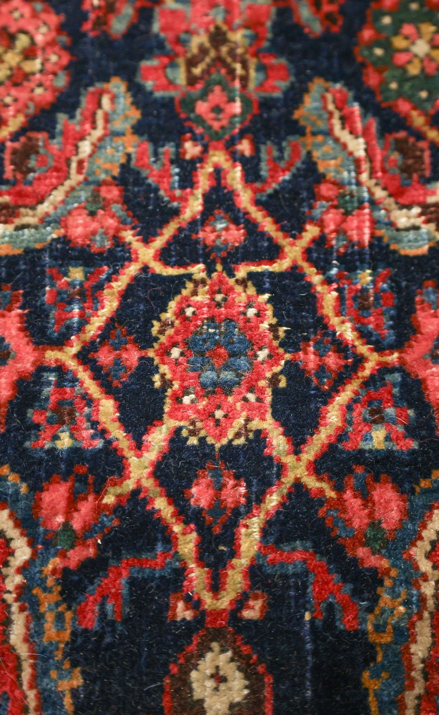 Close-up of antique rug detail, showcasing intricate handwoven pattern in deep blues and reds.
