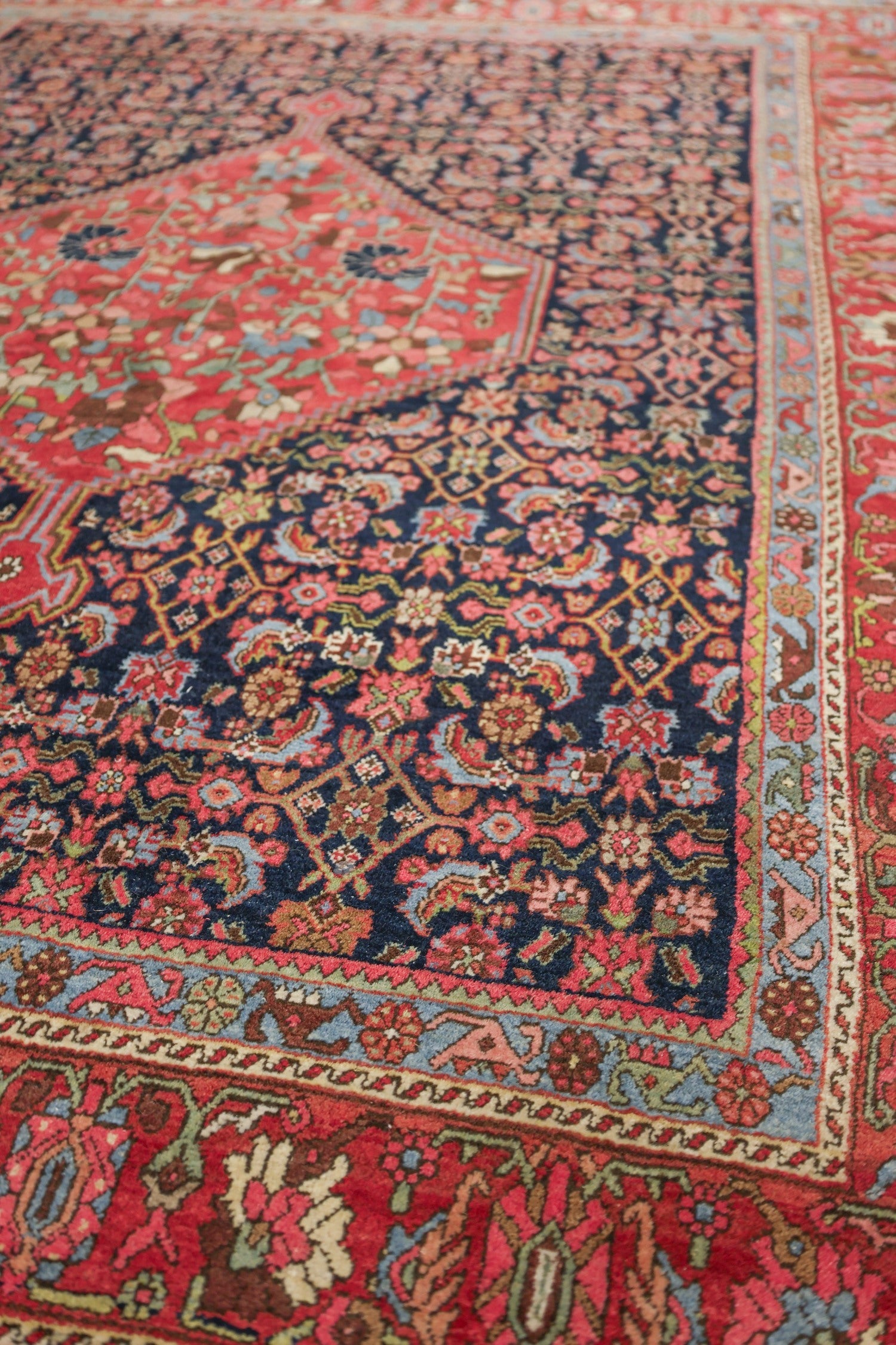 Detail of antique Bijar rug, showcasing intricate floral patterns in red, blue, and ivory.
