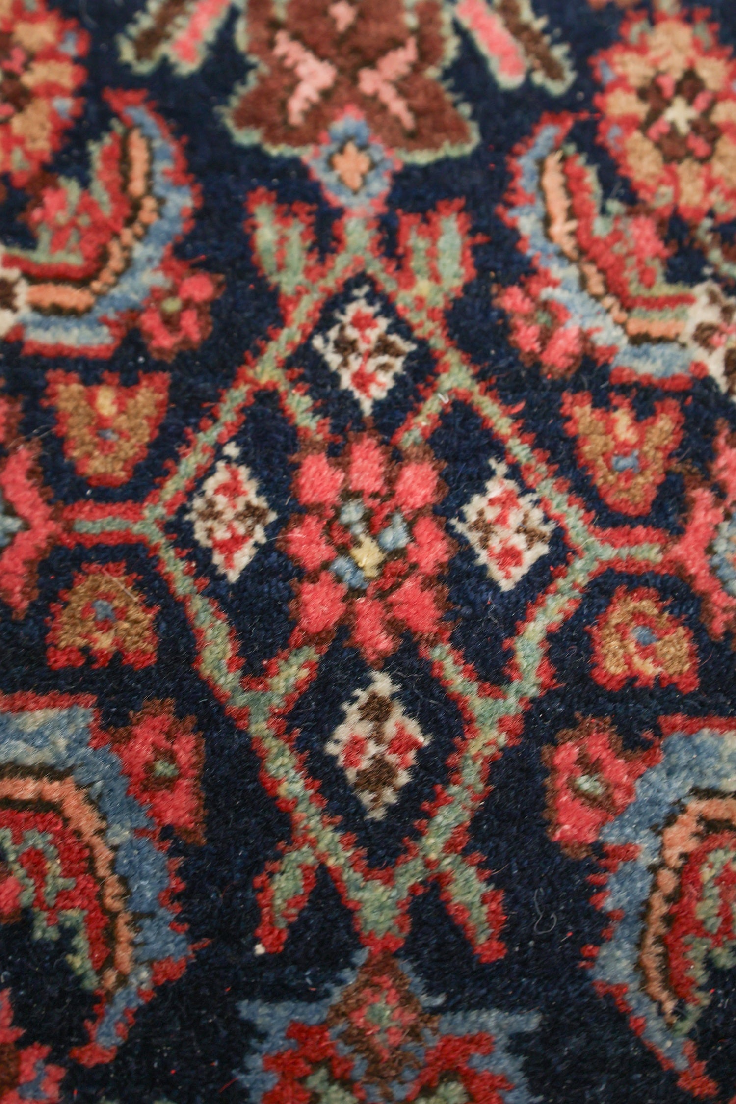 Close-up view of a richly colored, handwoven rug with intricate floral patterns in red, blue, and beige tones.
