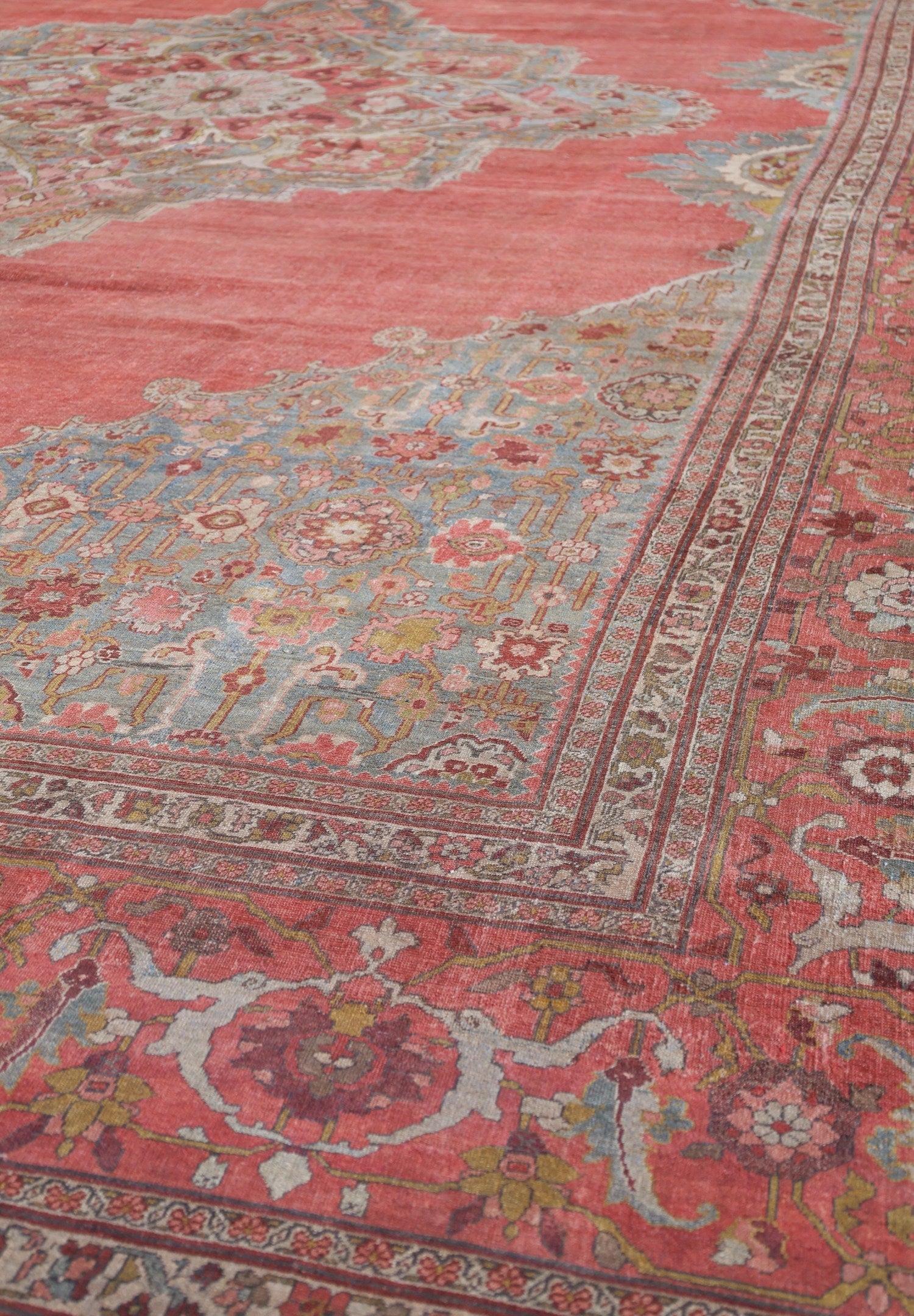 Close-up of a vintage rug's intricate design, featuring faded pinks, blues, and greens in a floral pattern.
