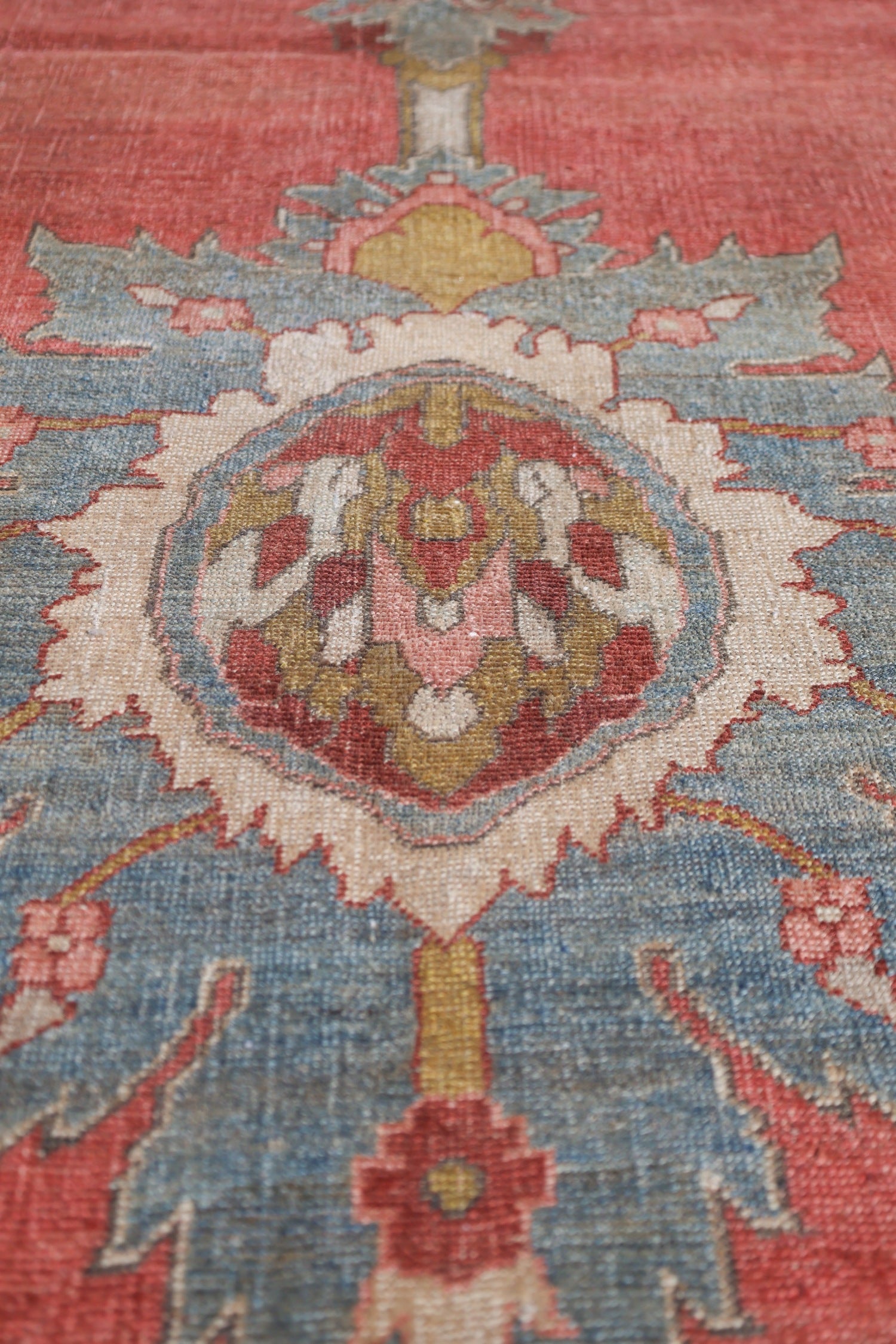 Close-up detail of a vintage rug's handwoven design, showcasing muted reds, blues, and creams in an intricate pattern.
