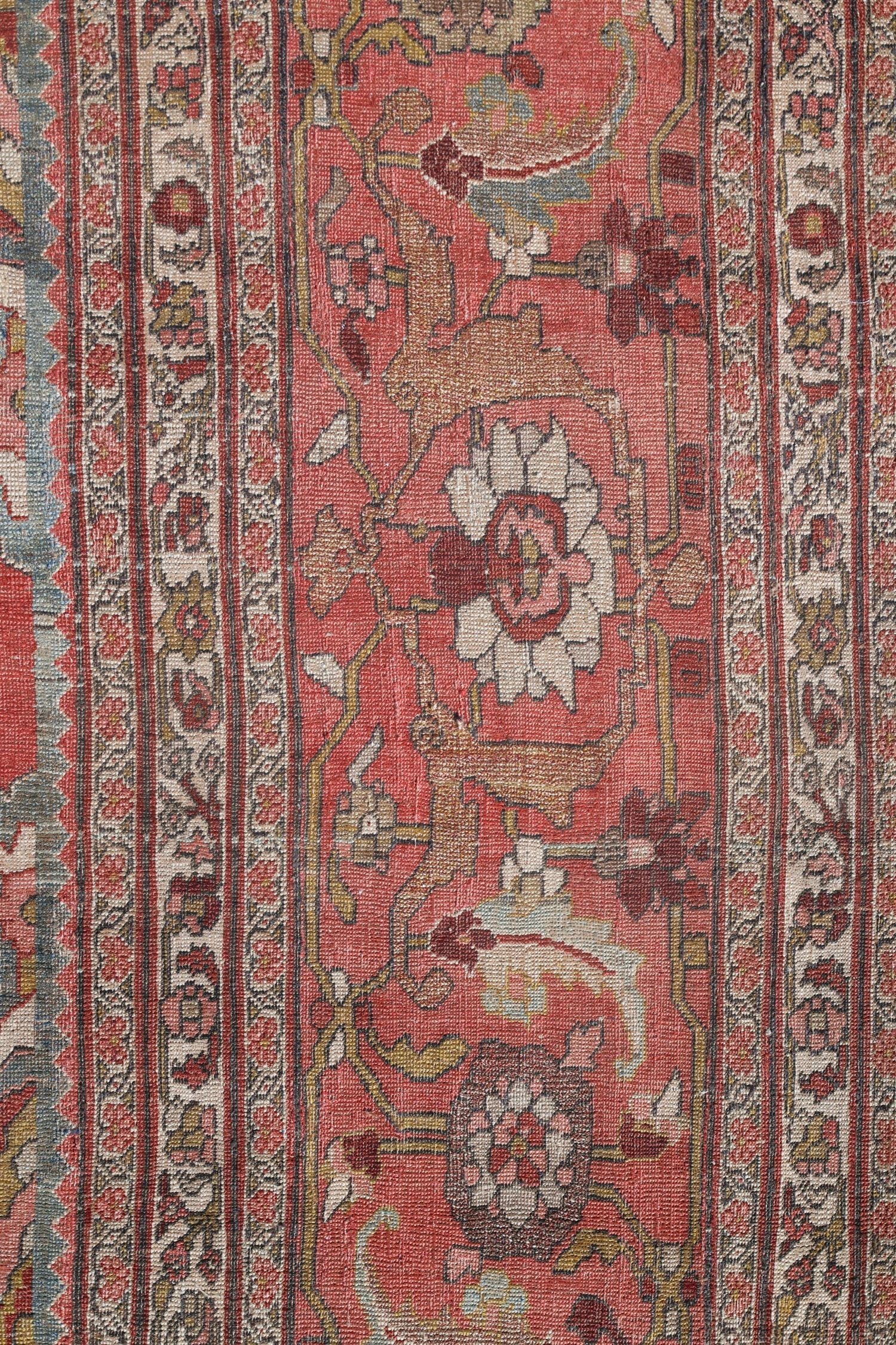 Detail of antique Bijar rug, showcasing handwoven floral patterns in muted reds and creams.
