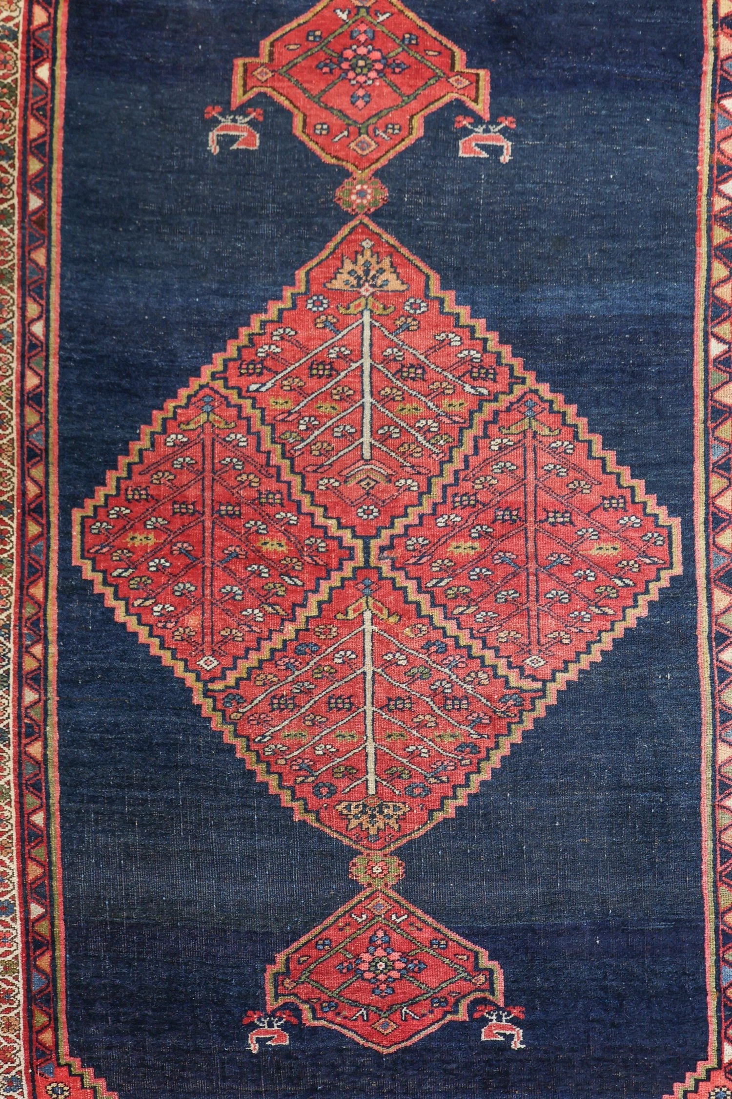 Detail of antique rug's handwoven, dark blue field with a central red diamond pattern.
