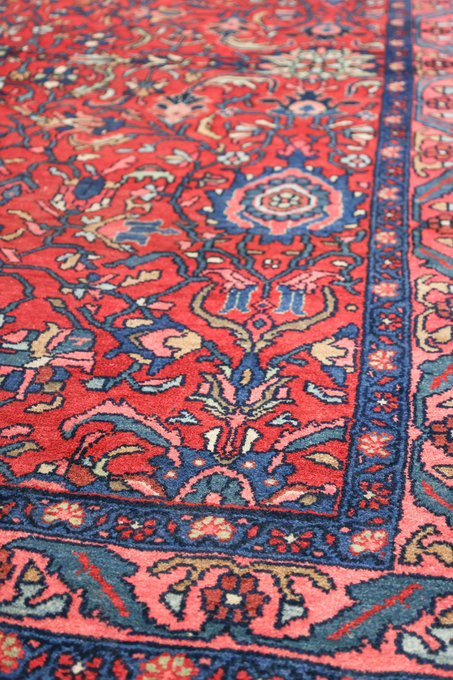 Detail of a handwoven rug with a red background and intricate blue and floral patterns.
