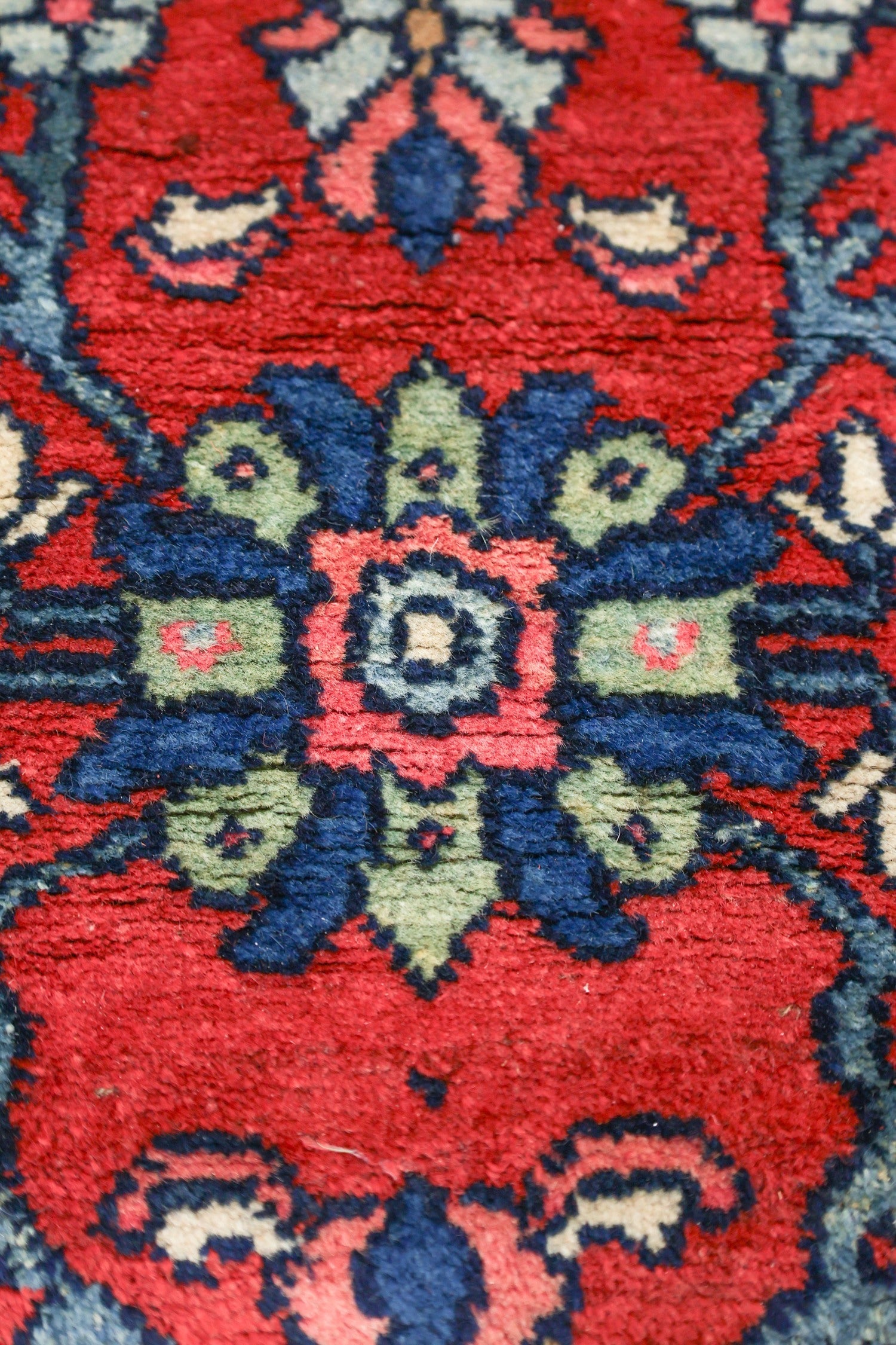 Close-up of antique rug detail; vibrant red, blue, and green floral pattern, handwoven texture.
