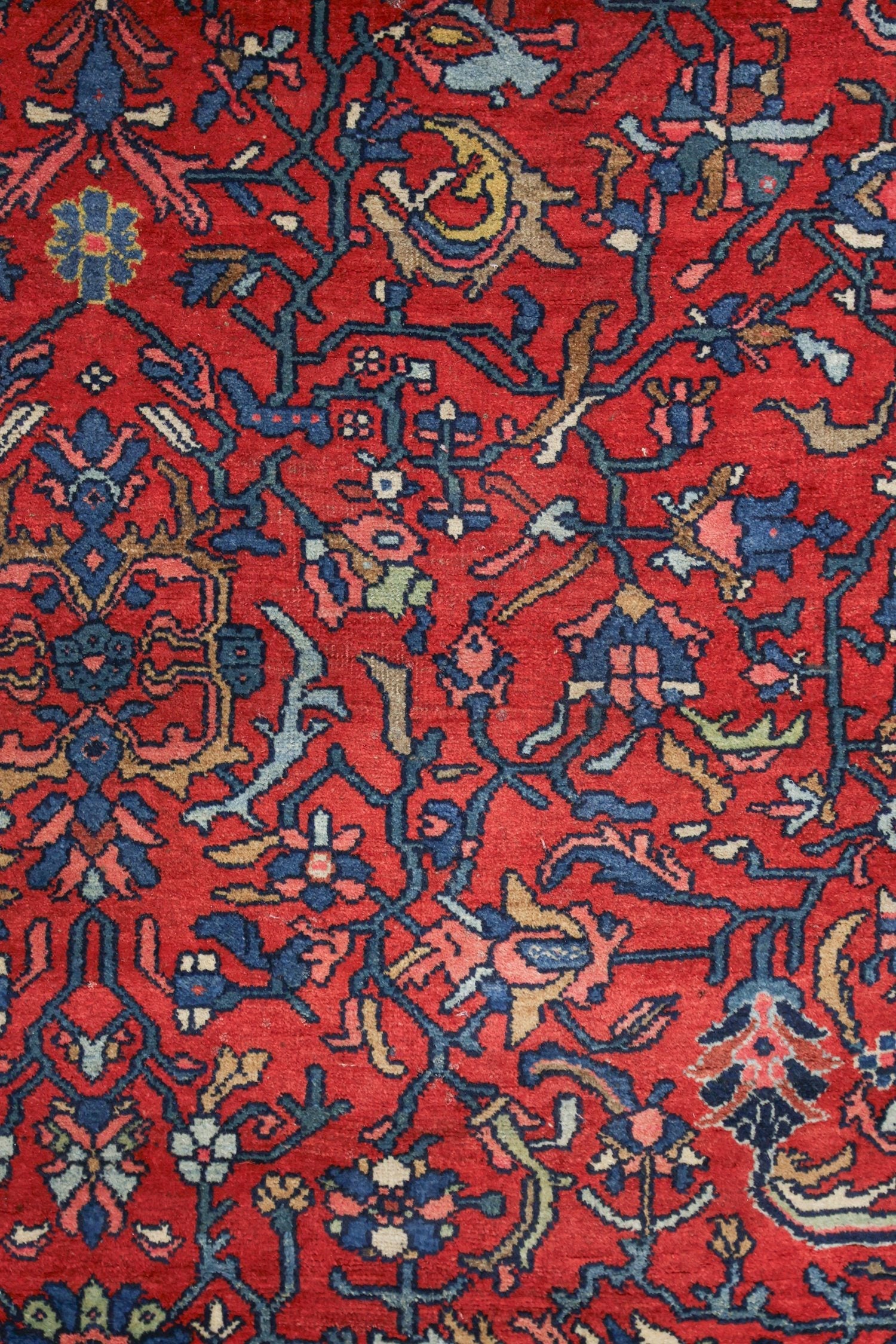 Close-up of a red antique rug with intricate floral and vine patterns in blue, beige, and ivory.
