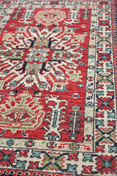 Handwoven Kazak rug detail: Red, cream, teal, and navy geometric pattern.
