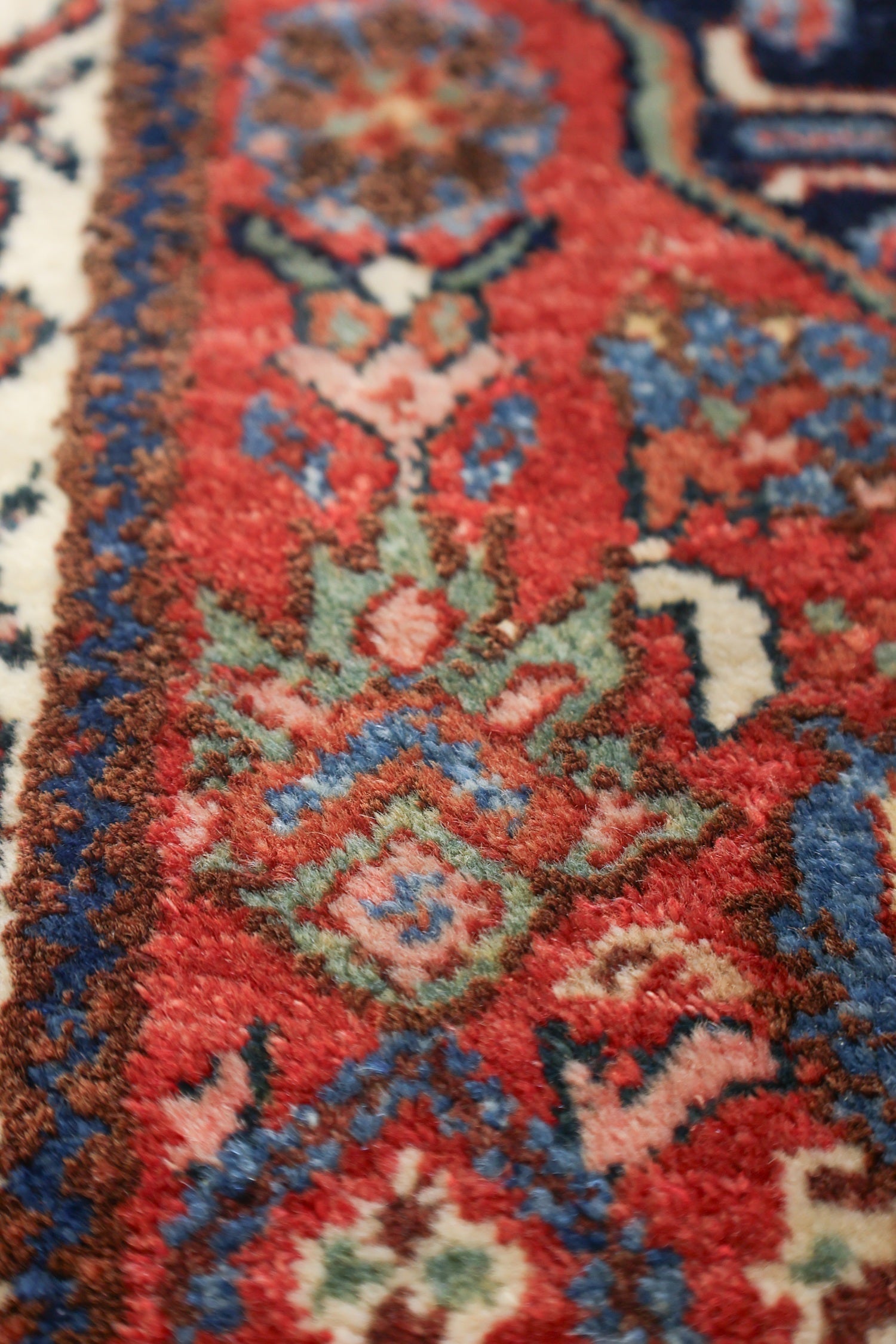 Close-up of handwoven rug detail; rich reds, blues, and creams in a tribal pattern.
