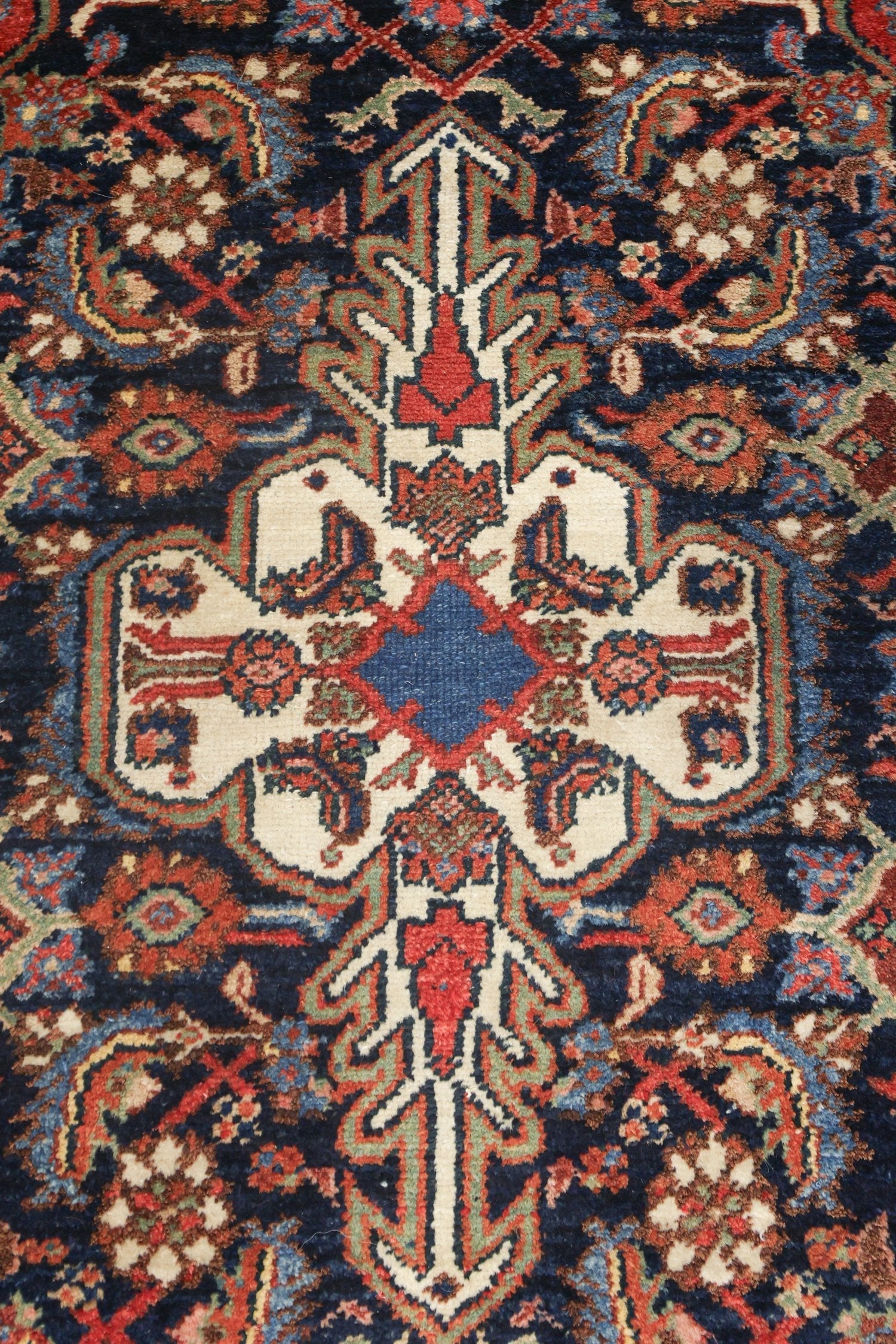 Intricate detail of an antique handwoven rug, showcasing a rich navy blue backdrop with red, cream, and green floral patterns.
