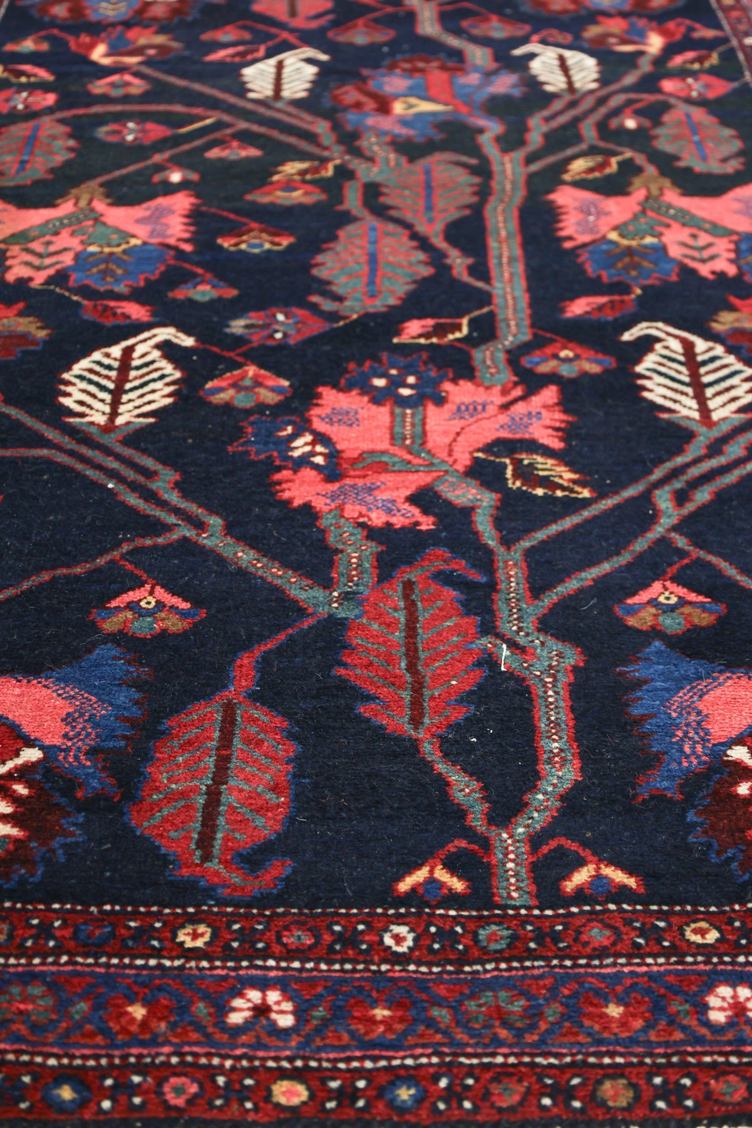 Close-up of a dark blue antique rug with a detailed floral pattern in shades of red and green.
