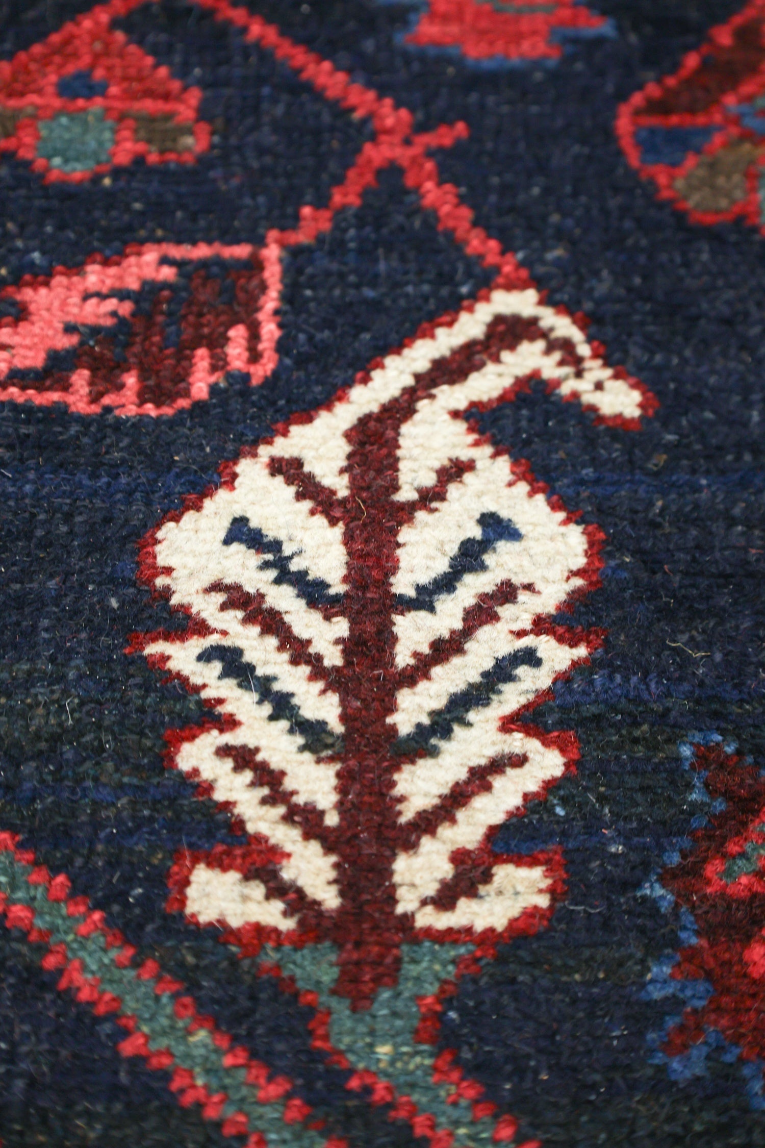 Close-up of a handwoven rug detail, showing intricate red, white, and navy blue floral pattern.
