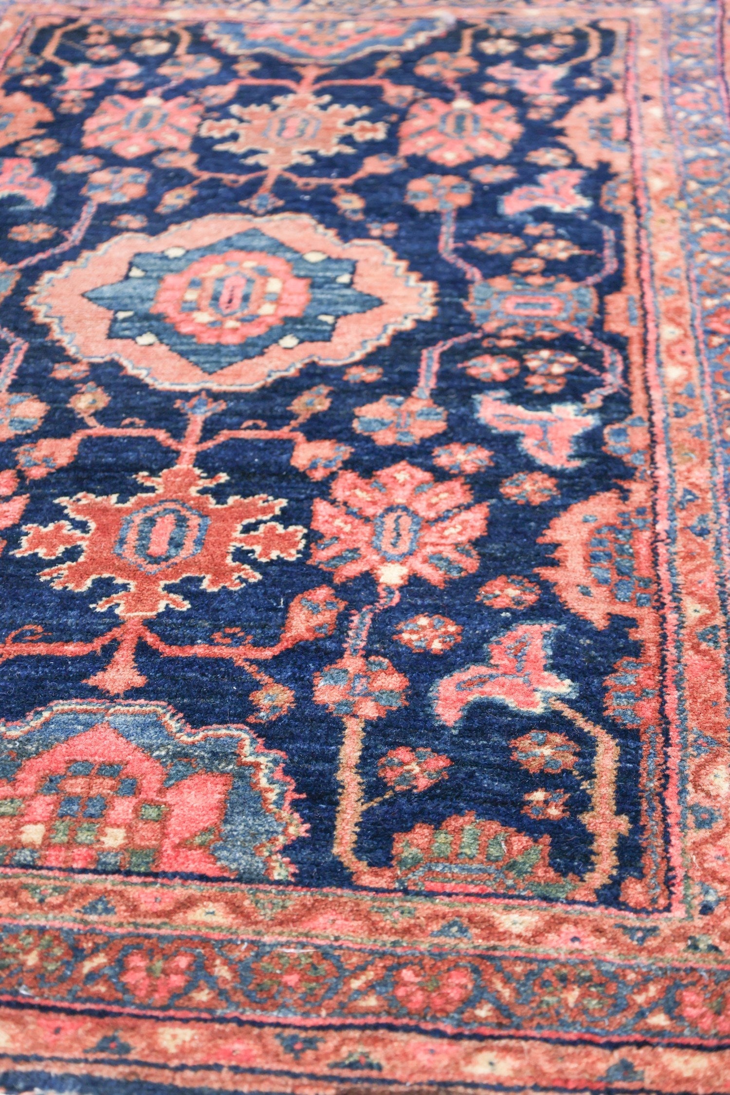 Detailed close-up of a vintage handwoven rug with a navy blue and coral floral pattern.
