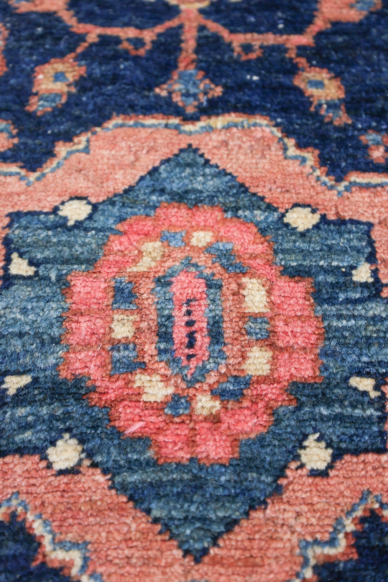 Close-up of antique rug detail, showcasing intricate handwoven pattern in muted pink and blue tones.
