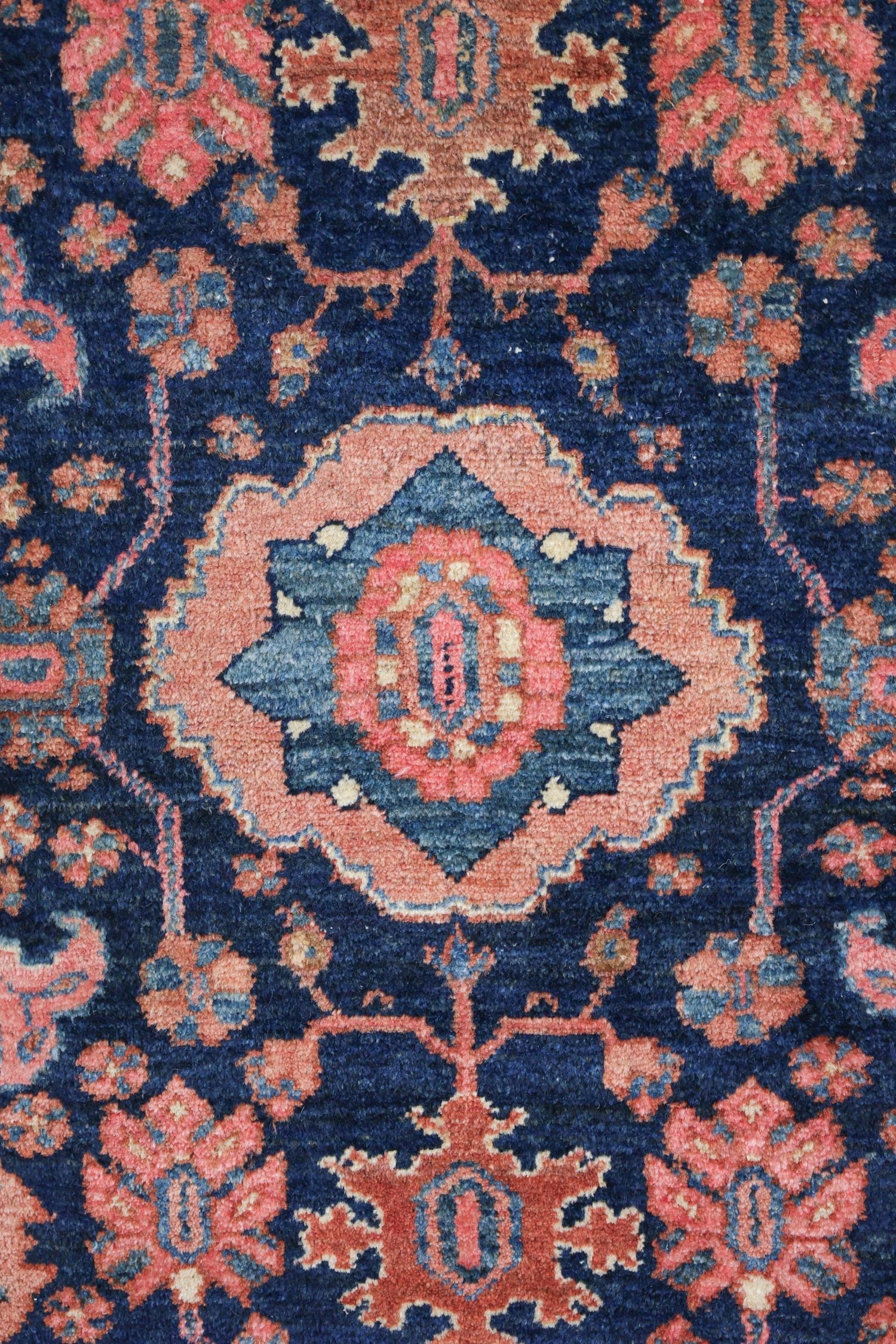 Close-up of antique handwoven rug, deep blue and coral floral pattern.
