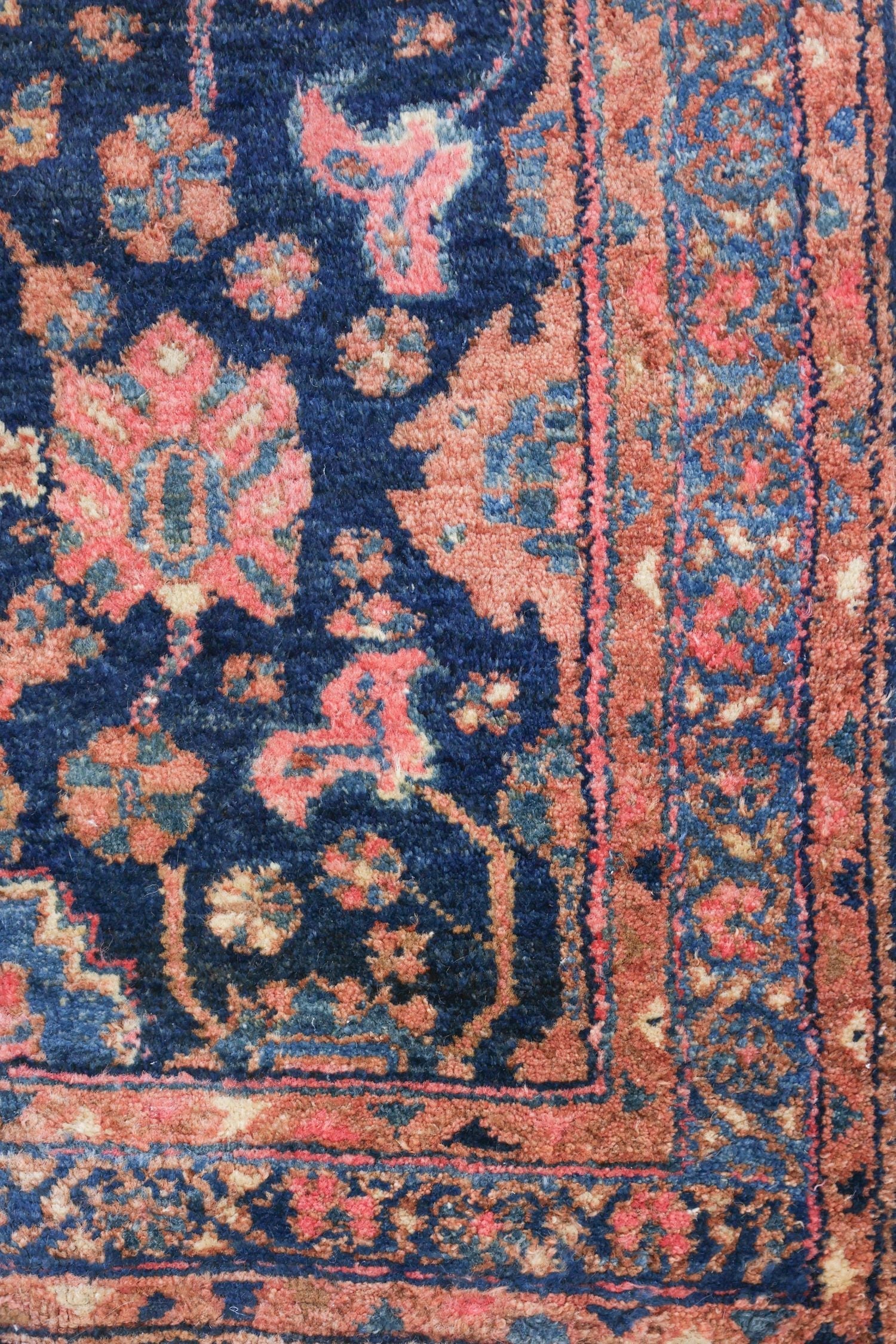 Close-up of antique rug's detailed, handwoven pattern in deep blues and muted pinks.
