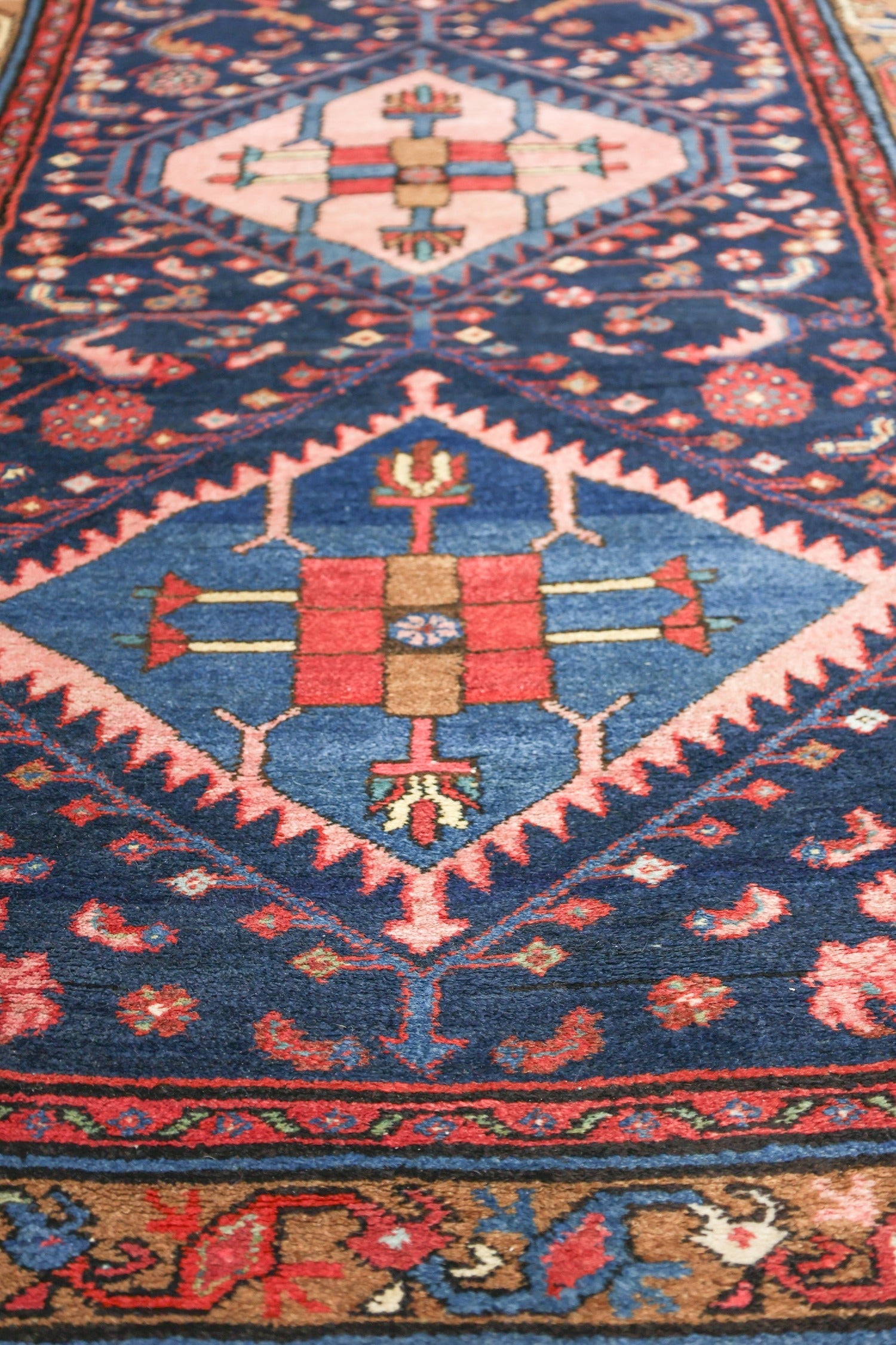 Close-up detail of a handwoven rug, showcasing vibrant blues, reds, and pinks in a geometric tribal design.
