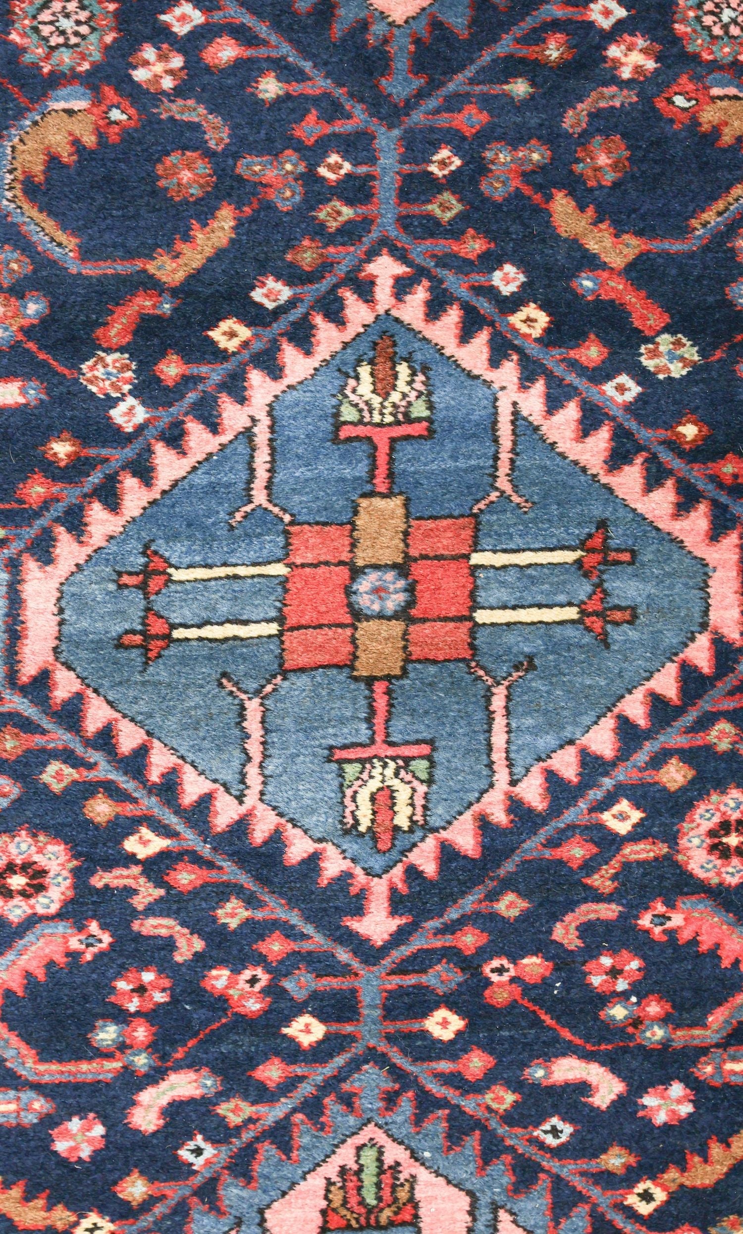 Detail of antique rug's handwoven floral pattern in navy, red, and pink.
