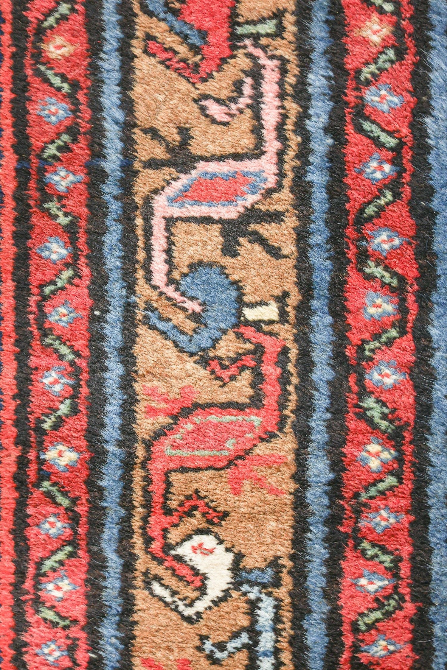 Close-up of antique rug detail, showing handwoven wool with red, blue, and beige patterns.
