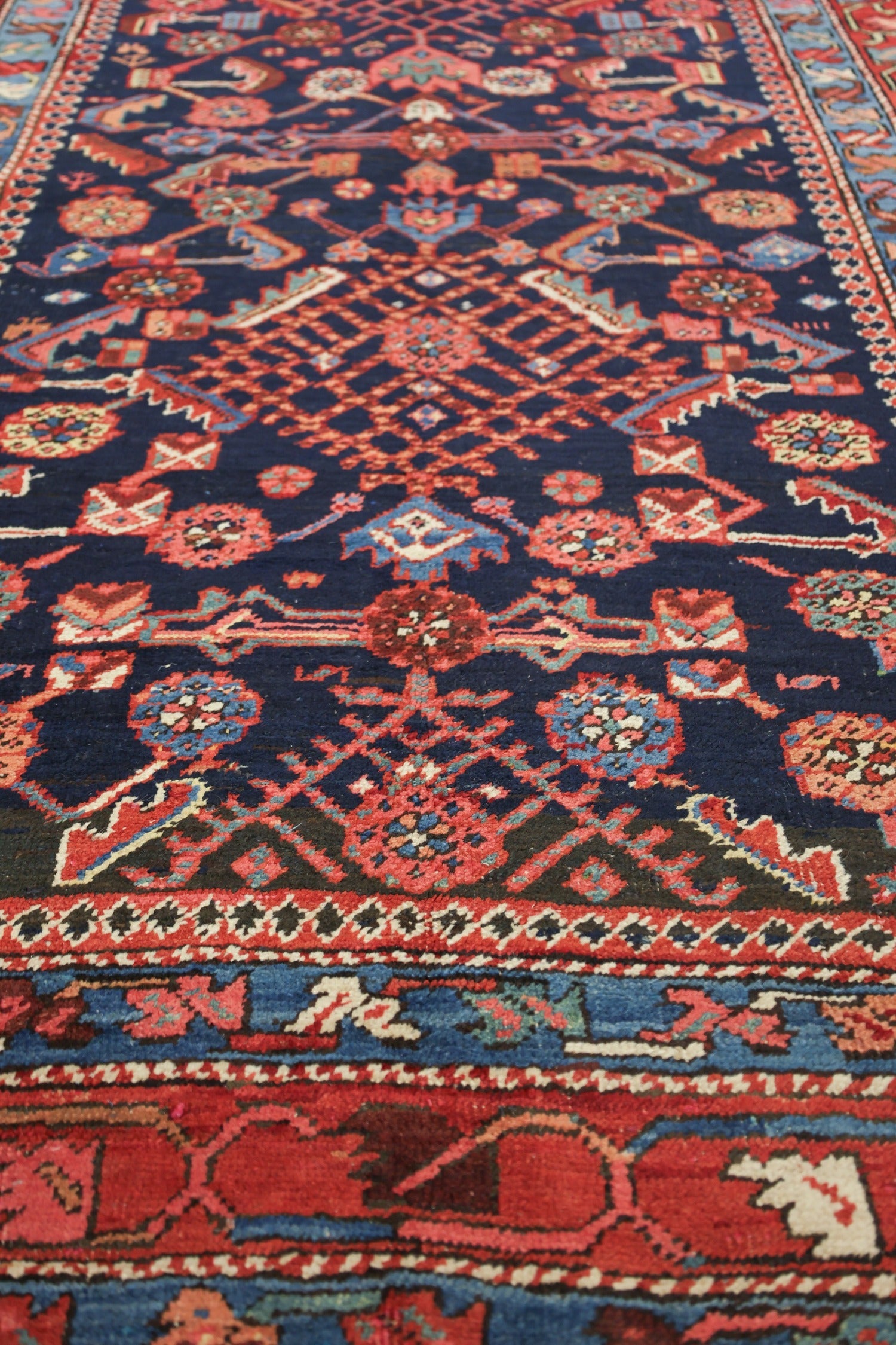 Detail of antique Heriz rug, showcasing vibrant red and blue tribal patterns on a dark navy background.
