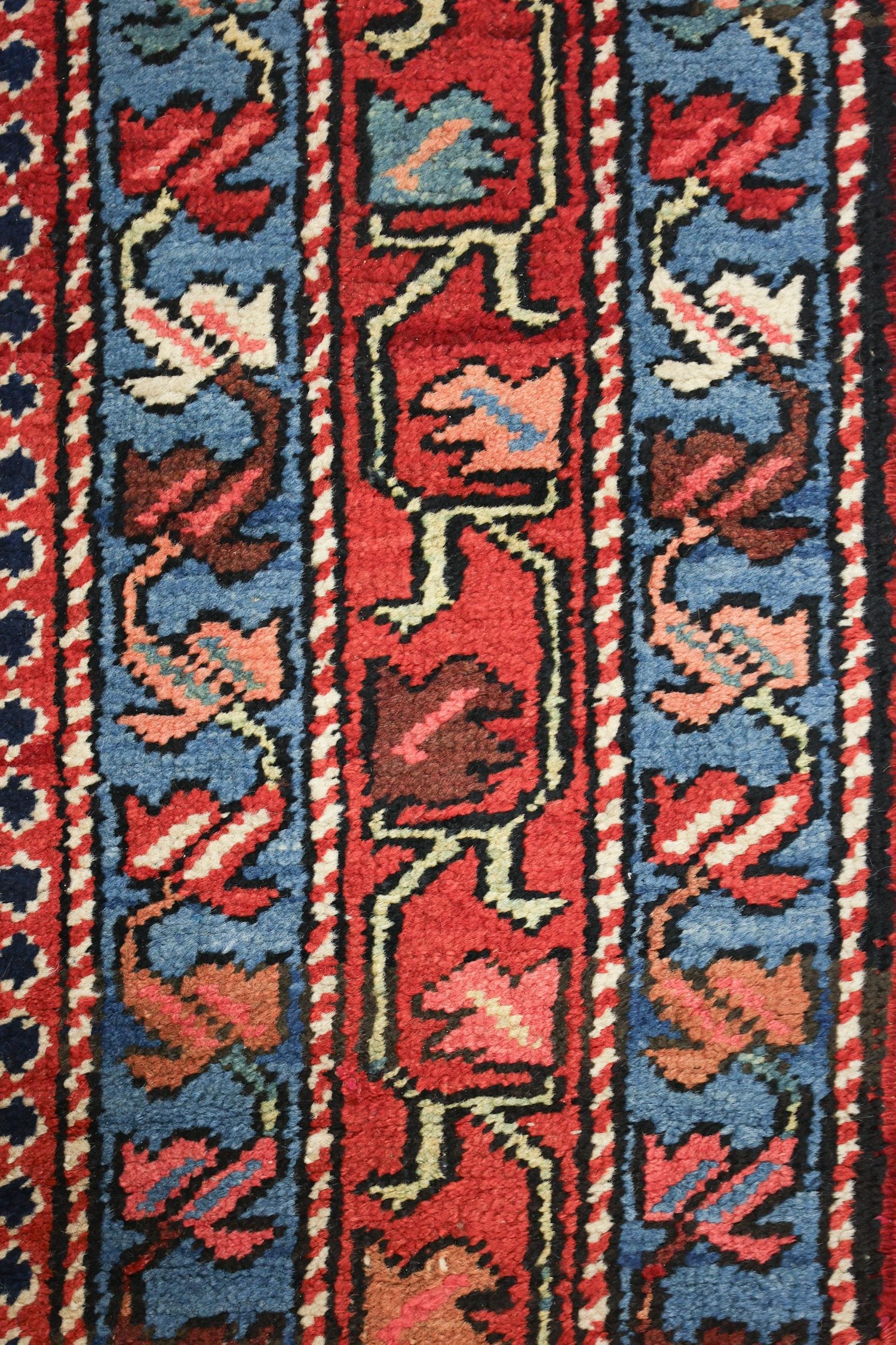 Close-up of handwoven Heriz rug detail, showcasing intricate floral pattern in red, blue, and beige.
