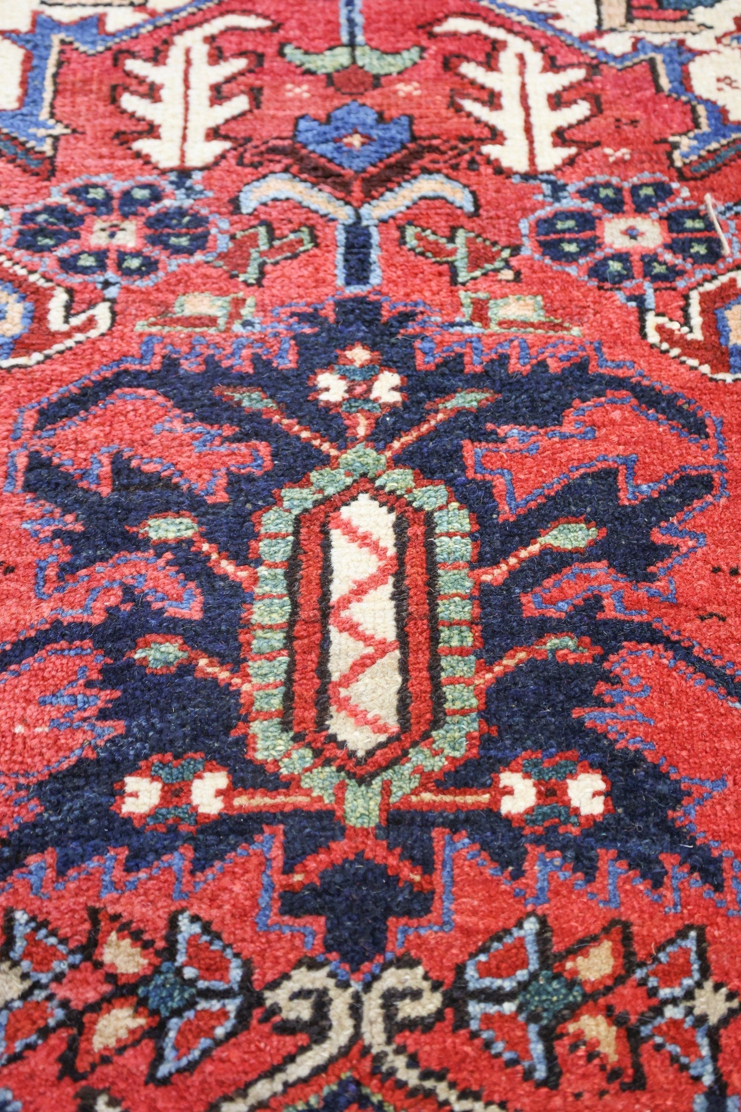 Intricate detail of a handwoven rug, showcasing a vibrant red base with navy, blue, and cream patterns.
