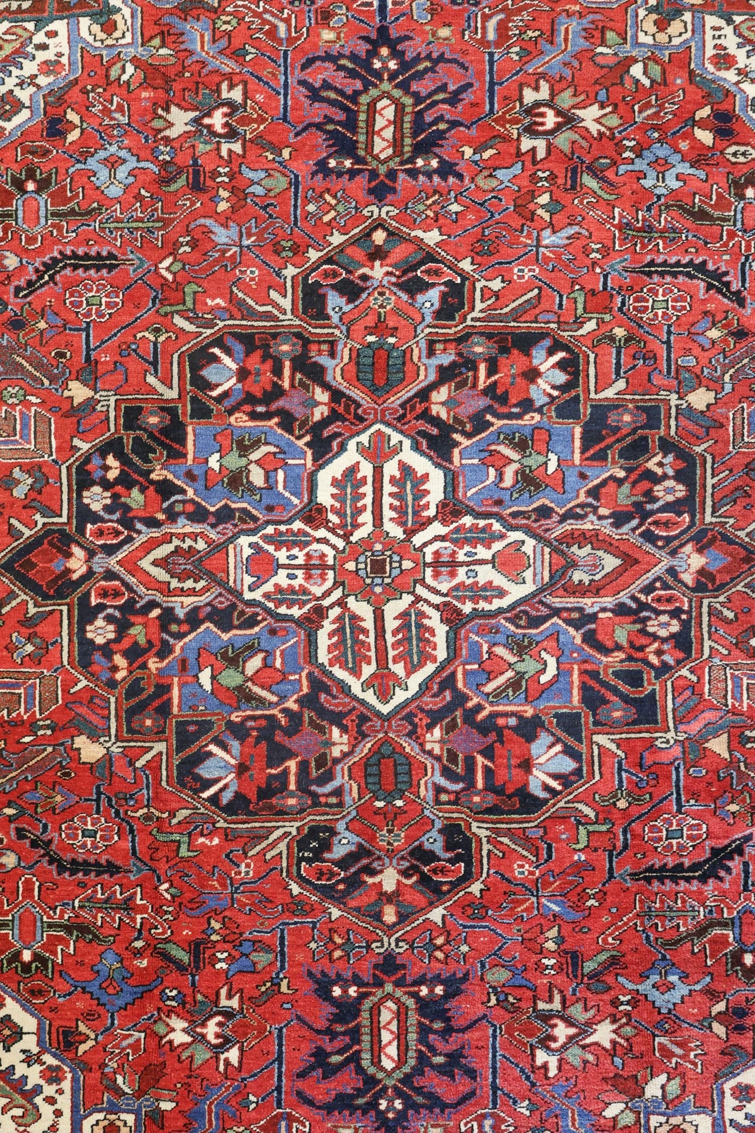 Intricate detail of a handwoven Heriz rug, showcasing a vibrant red base with a medallion design in navy, blue, and beige.
