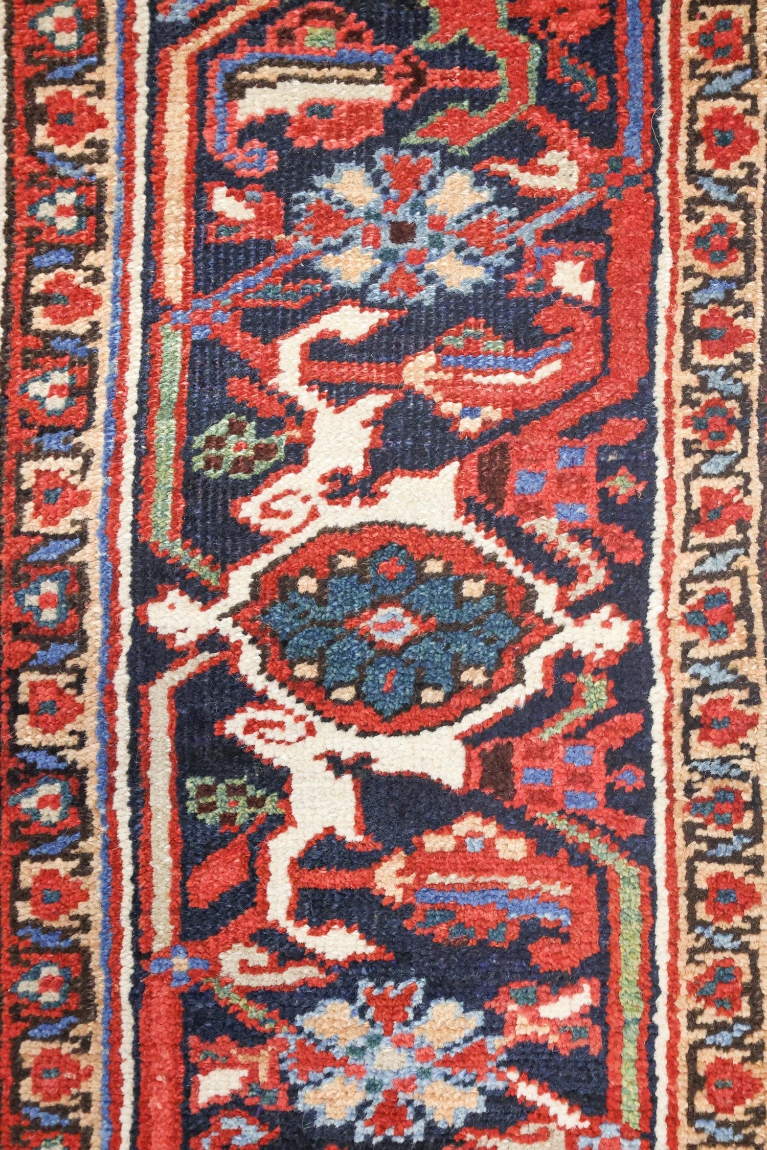 Close-up detail of a handwoven rug, showcasing intricate red, blue, and cream patterns.
