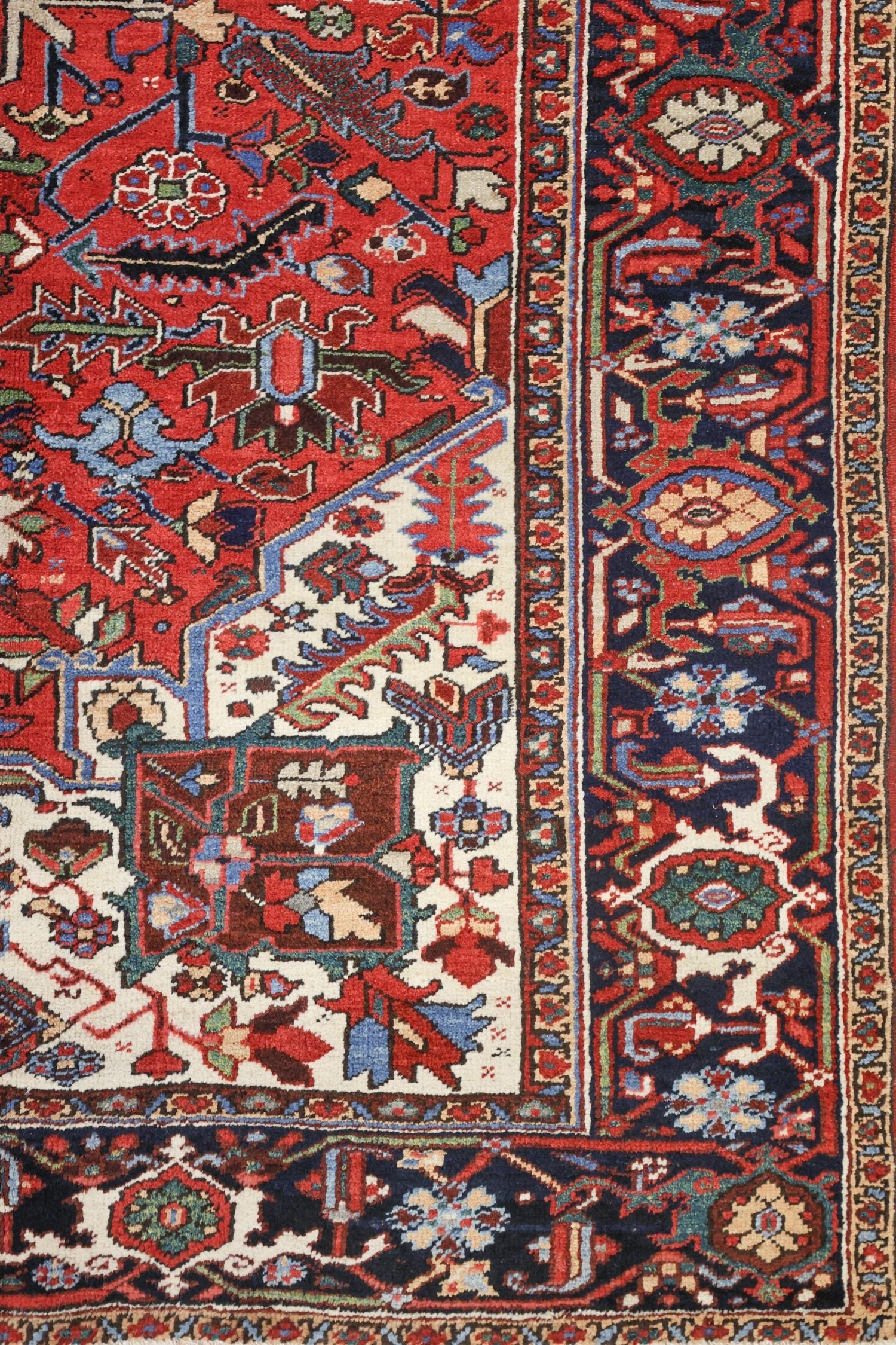 Detail of a handwoven Heriz rug, showcasing intricate floral and geometric patterns in red, blue, and ivory.
