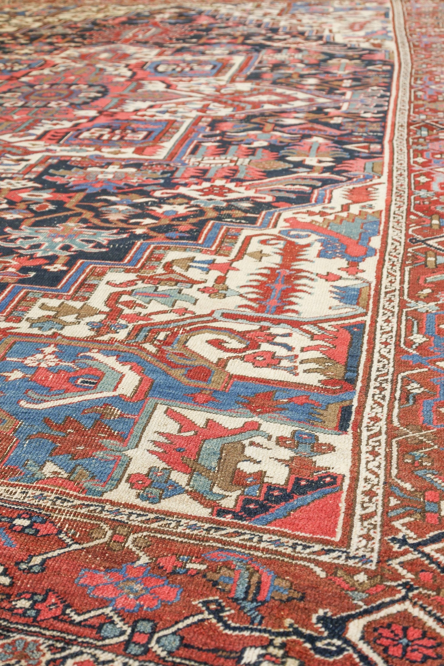 Handwoven Heriz rug detail, showcasing intricate tribal patterns in red, blue, and beige.
