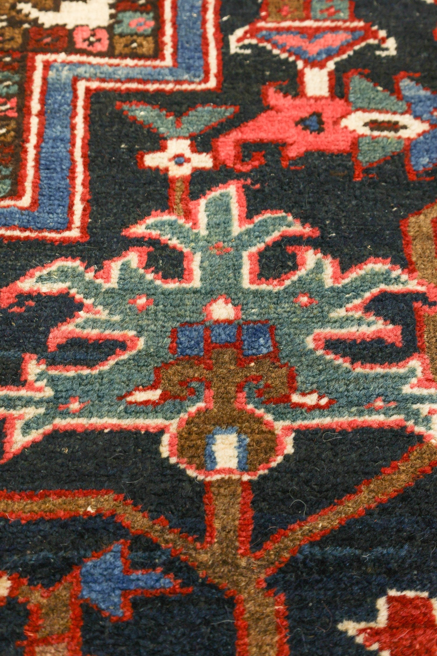 Close-up of a handwoven rug's intricate, multicolored pattern featuring teal, red, and brown details.
