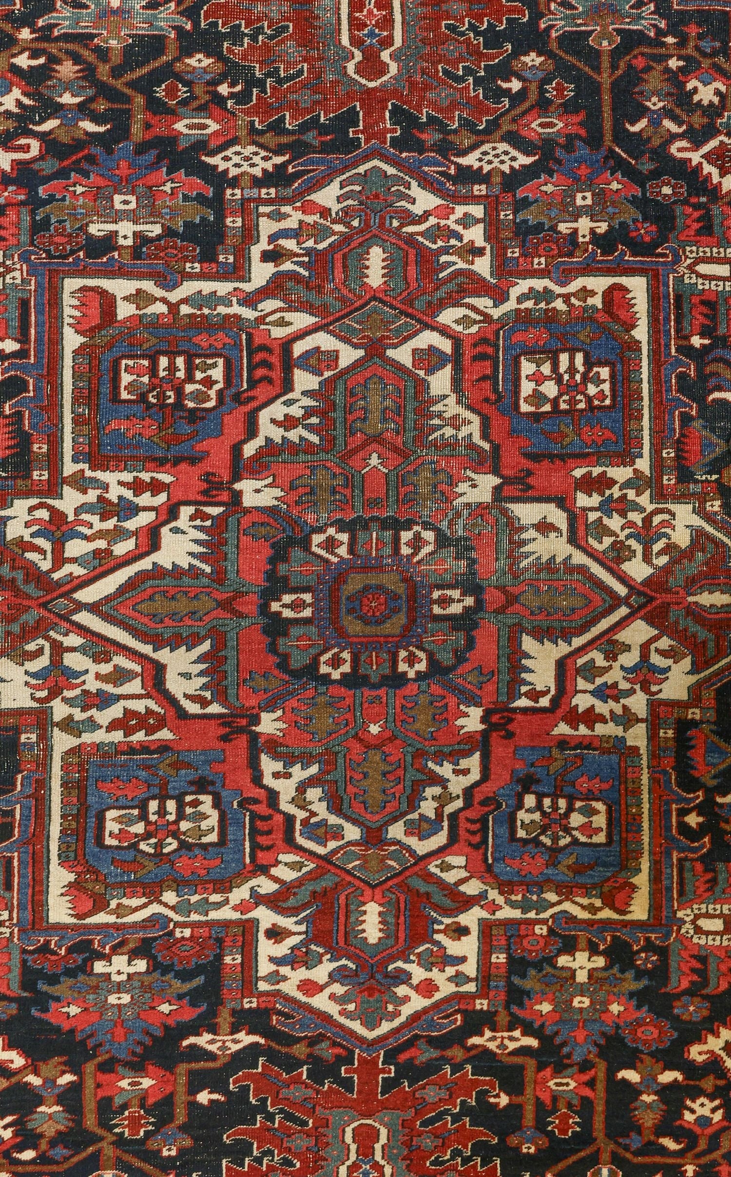 Intricate detail of an antique Heriz rug, showcasing rich reds, blues, and ivory in a traditional tribal pattern.
